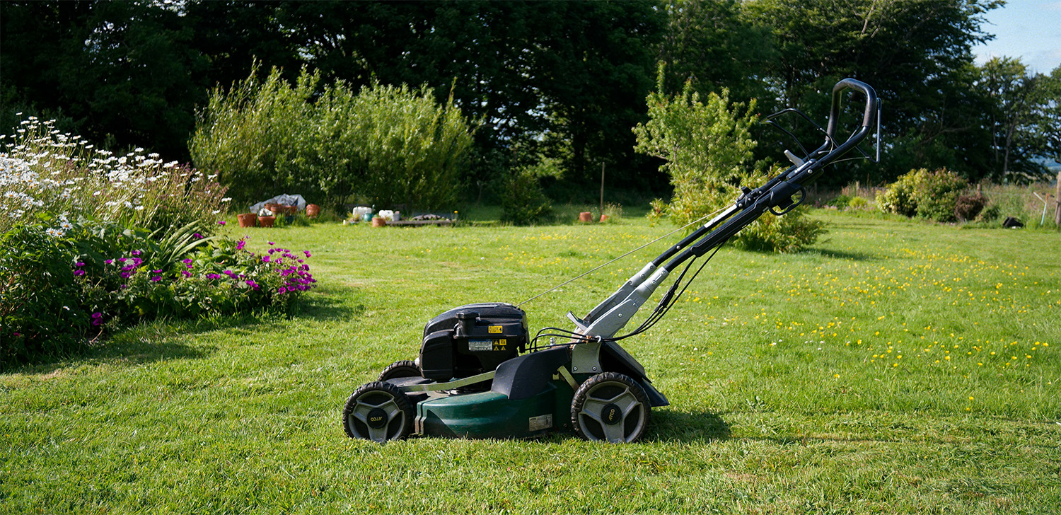 A lawn mower parked on a freshly cut lawn with trees and flowerbeds in the background, representing home and field service work in Forest Lake.