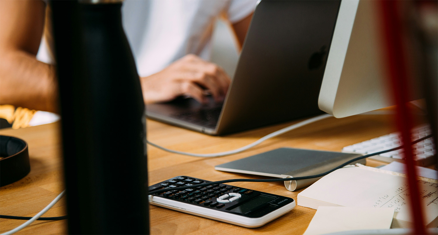Small business owner working on a laptop with calculator and notes nearby, showing the limitations of spreadsheets for bookkeeping.