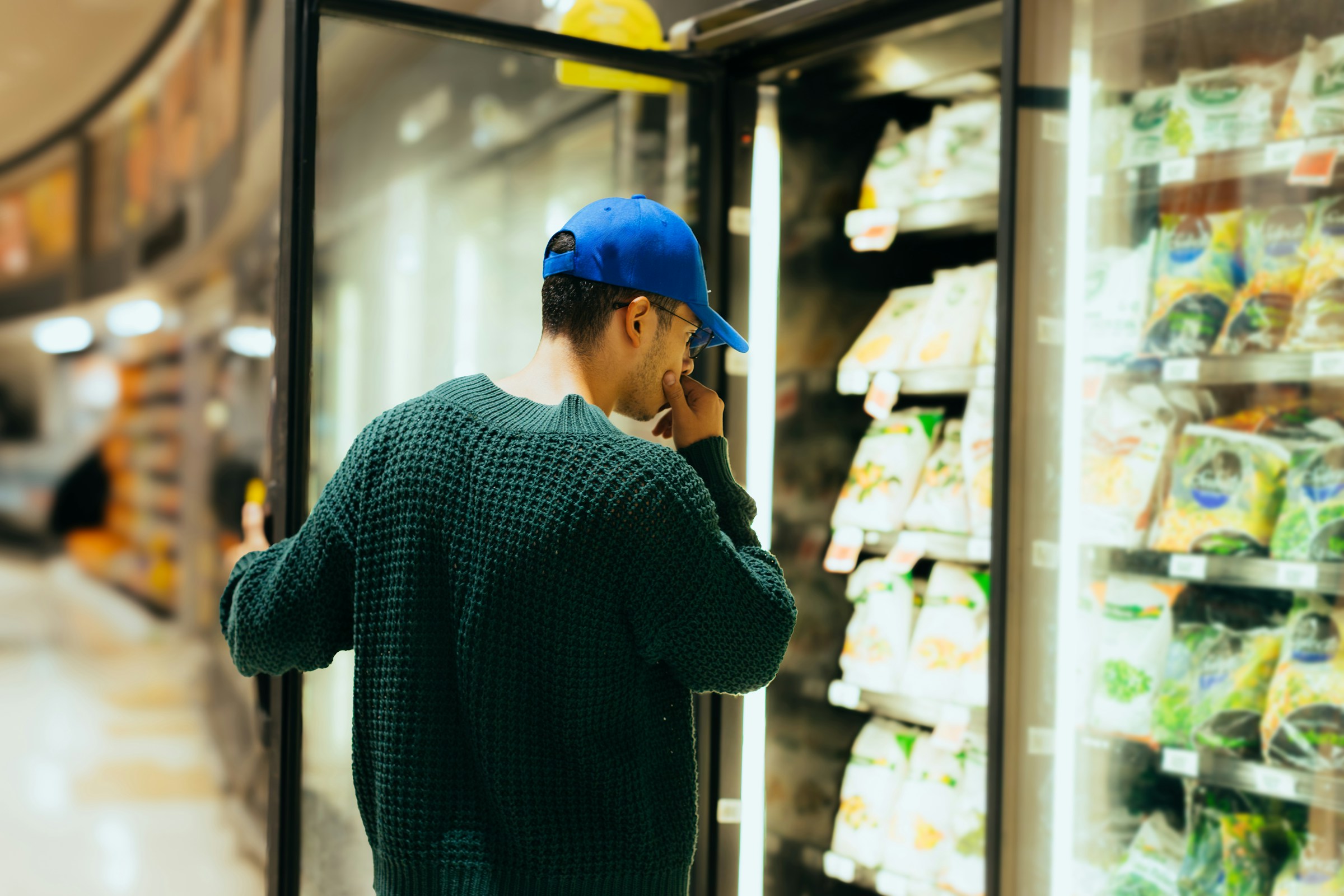 A man deciding while standing in front of a refrigerated cooler in a grocery store.
