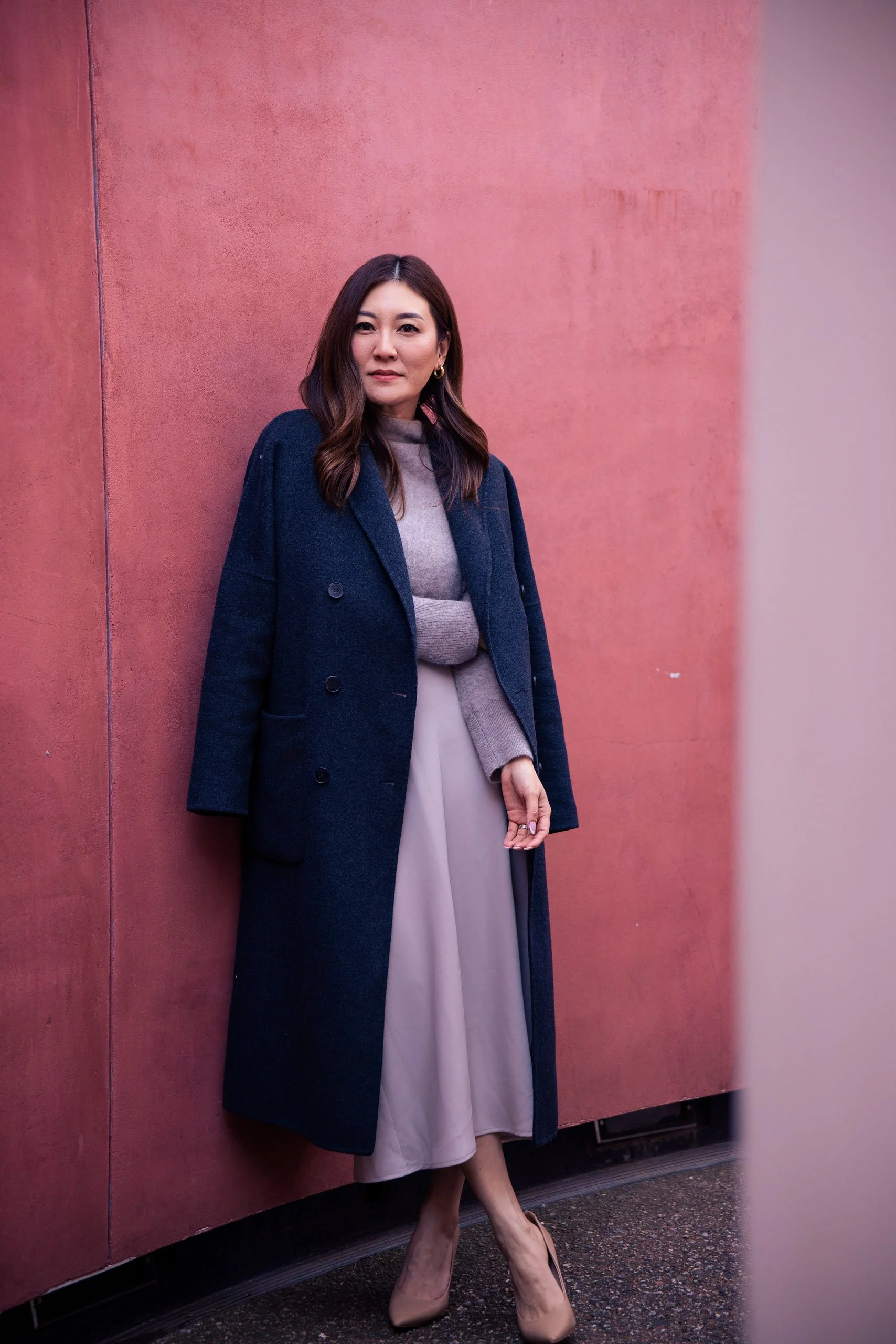 Portrait of a woman in a navy coat against a pink wall