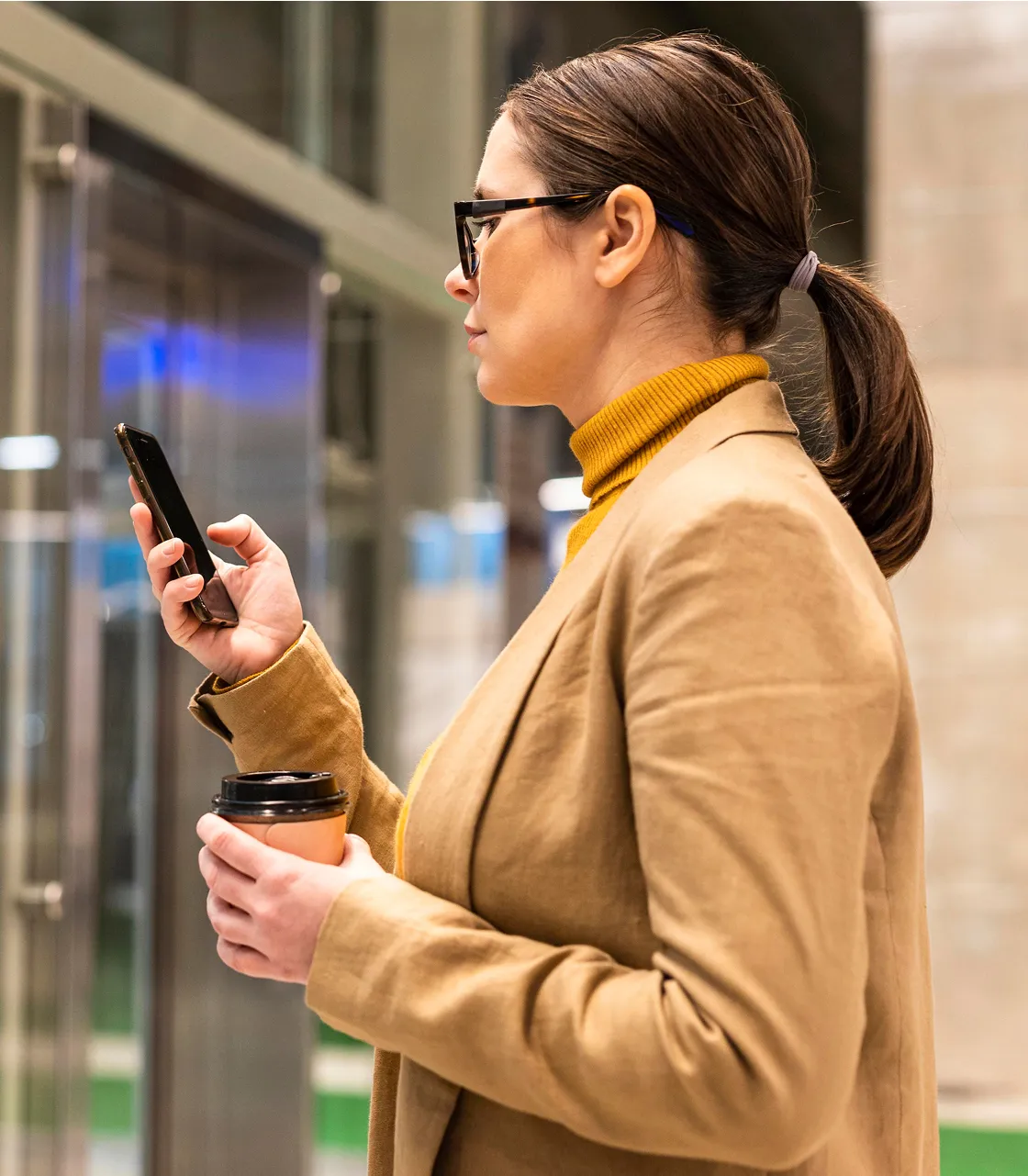 一个女人拿着杯子看着她的手机。