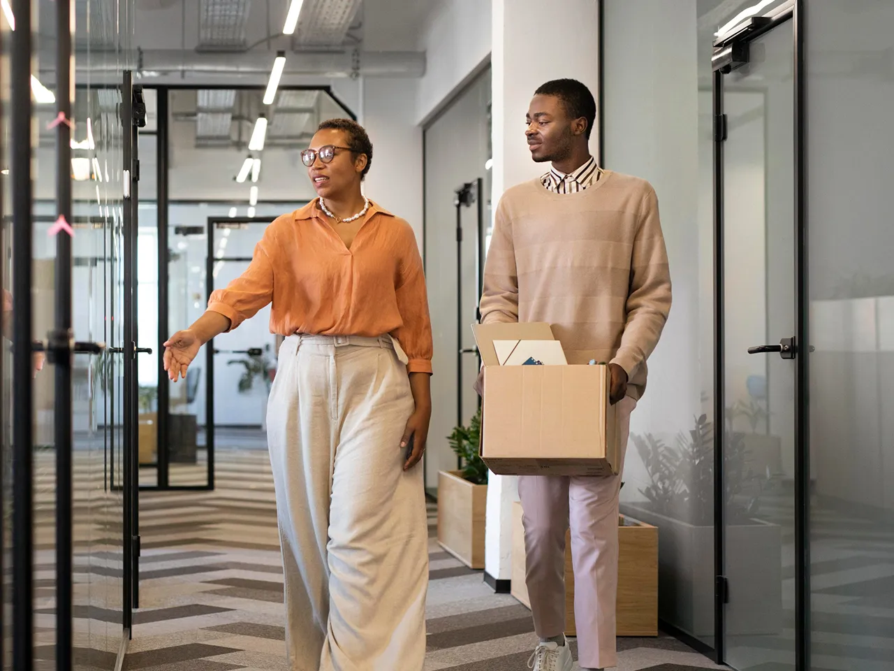 A man and woman walking together through a modern office building, engaged in conversation.