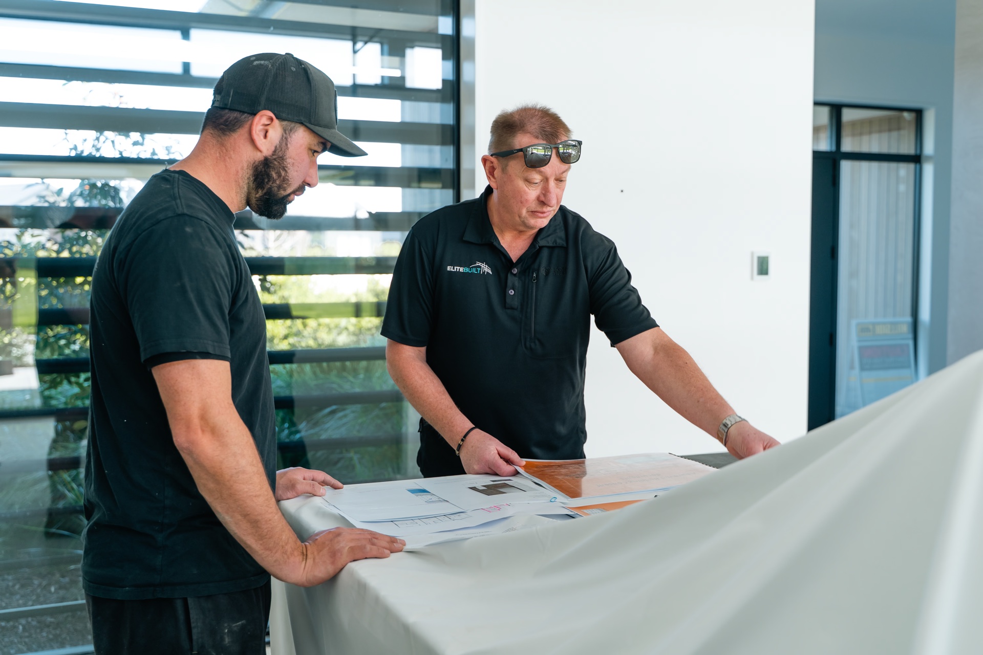 Two Elite Built team members reviewing plans on a bright residential site
