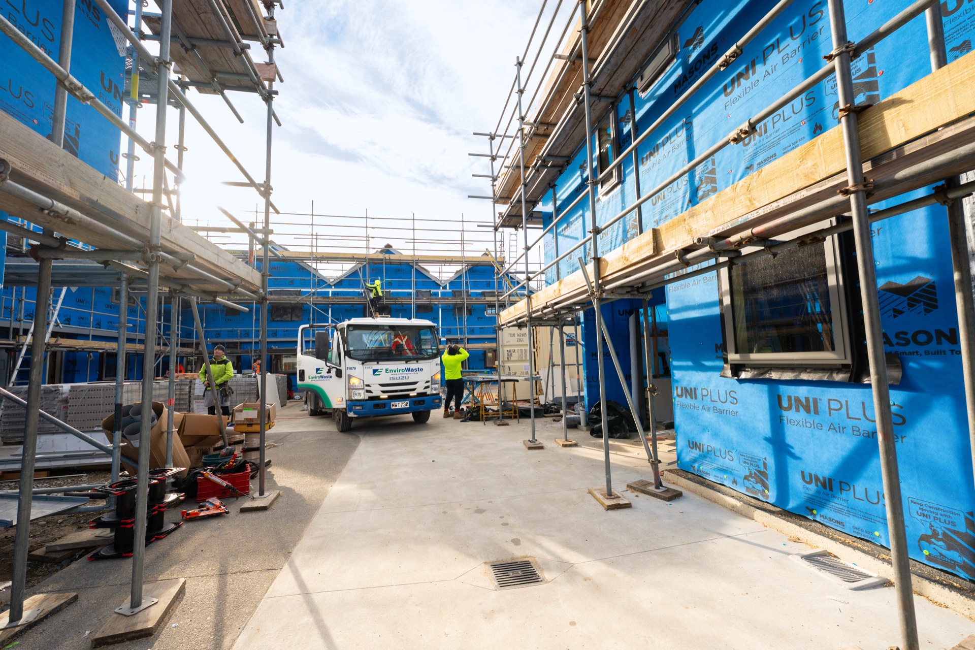 Townhouses under construction behind scaffolding with a truck and workers on site.