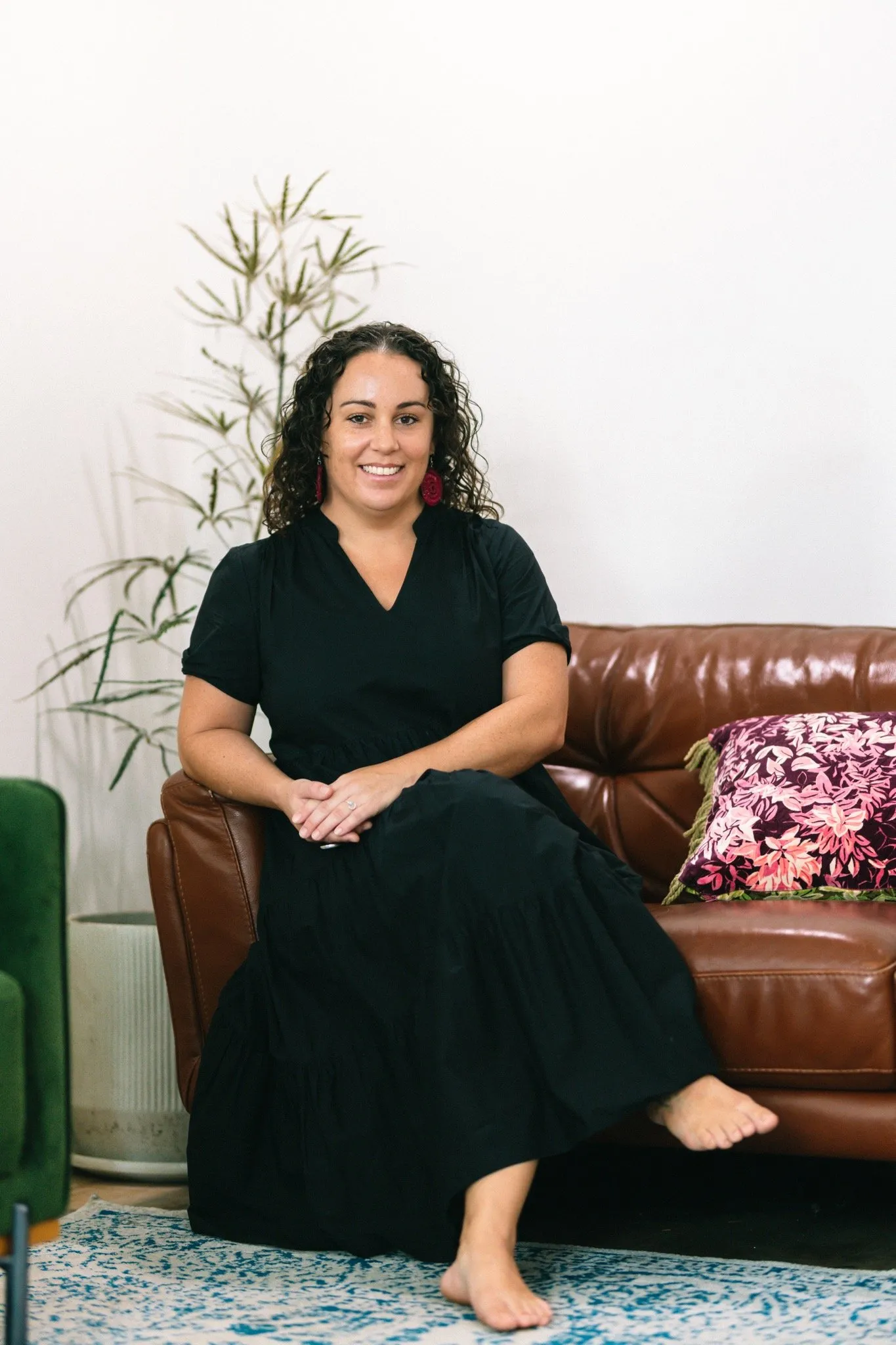 A woman in a black dress sitting on a brown couch.