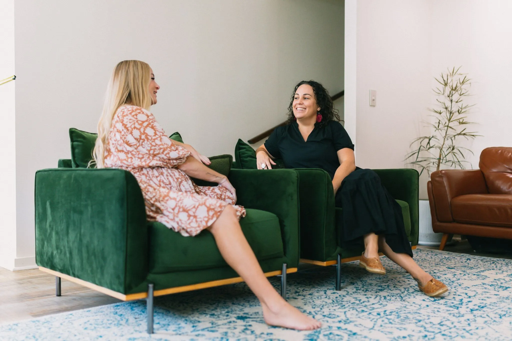 Two women sitting on green couches talking to each other.