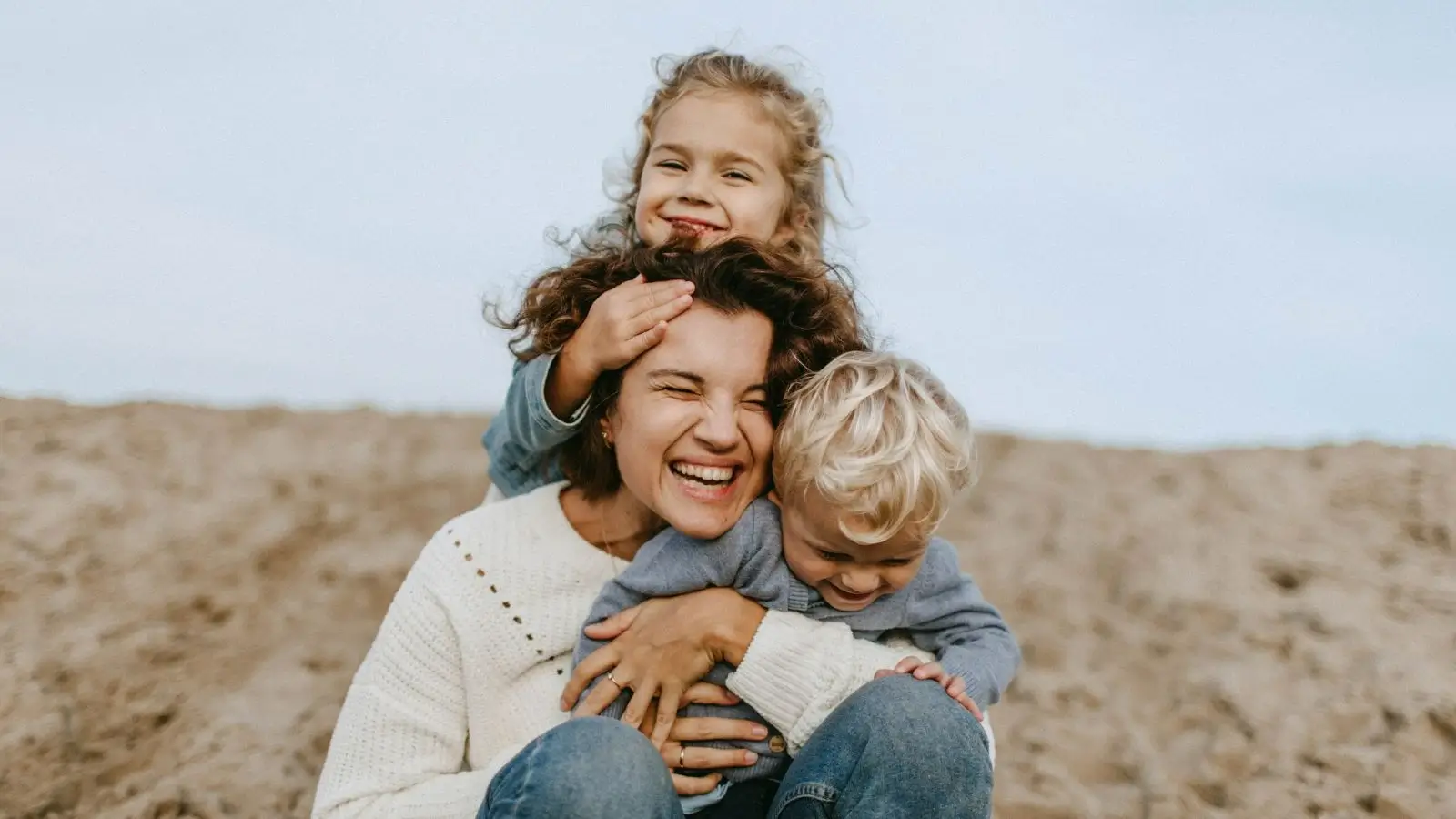A woman carrying and hugging her children and smiling