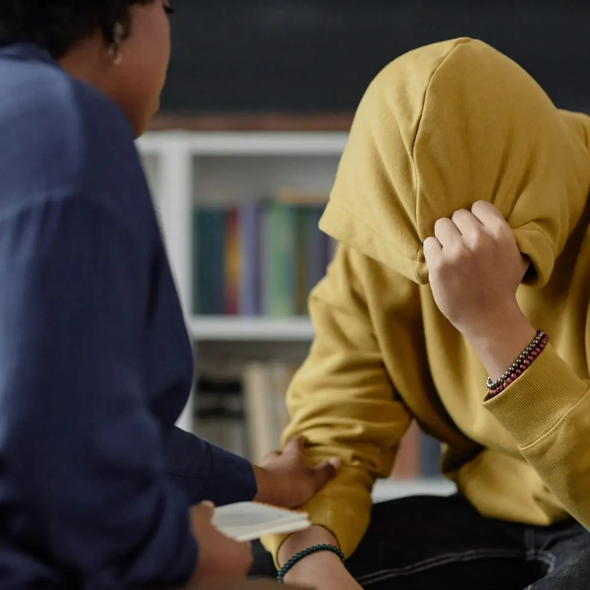 A teen wearing a jacket sitting on a chair while being comforted by a therapist
