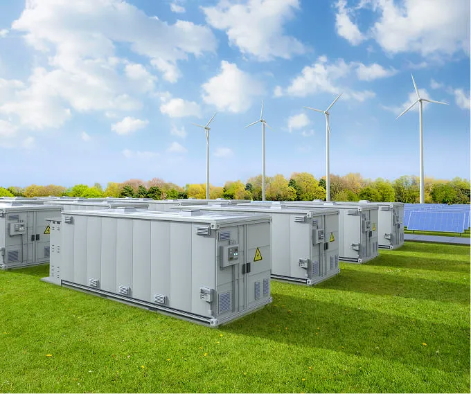A row of portable generators in a field with wind turbines in the background.