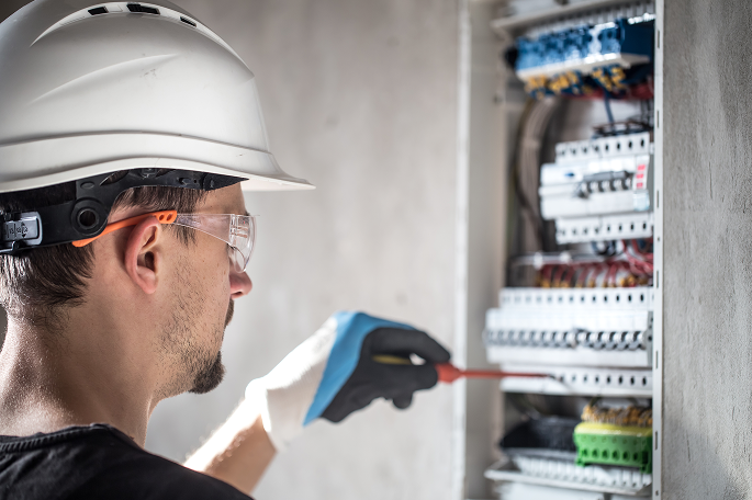 Elektroniker mit einem Schraubendreher vor einem Schaltschrank