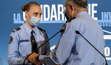 Deux gendarmes en uniforme et masque facial se serrent la main lors d'une cérémonie officielle.