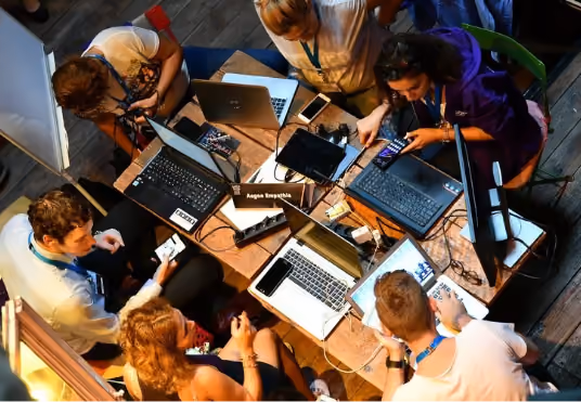 Groupe de six personnes travaillant ensemble autour d'une table avec ordinateurs portables et appareils mobiles.