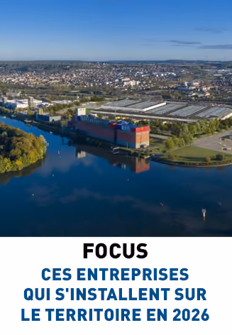 Vue aérienne d'une grande usine ou centre logistique bordant une rivière avec une ville en arrière-plan sous un ciel bleu dégagé, avec le texte en dessous indiquant «FOCUS CES ENTREPRISES QUI S’INSTALLENT SUR LE TERRITOIRE EN 2026».