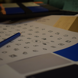 Close-up of a sheet with various small geometric symbols and a blue pen resting on it, with blurred color swatches in the background.