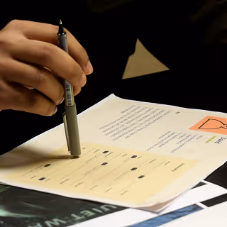Hand holding a pen marking answers on a printed multiple-choice test sheet.