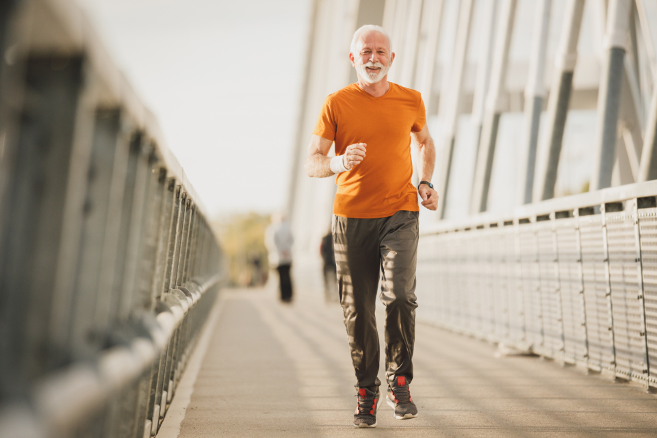 An older man jogging outdoors on a footbridge — Longevity & Healthspan