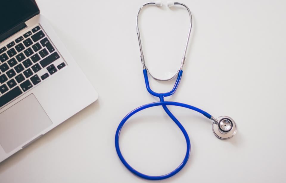A stethoscope beside a laptop in a clinical office — AI & Digital Health