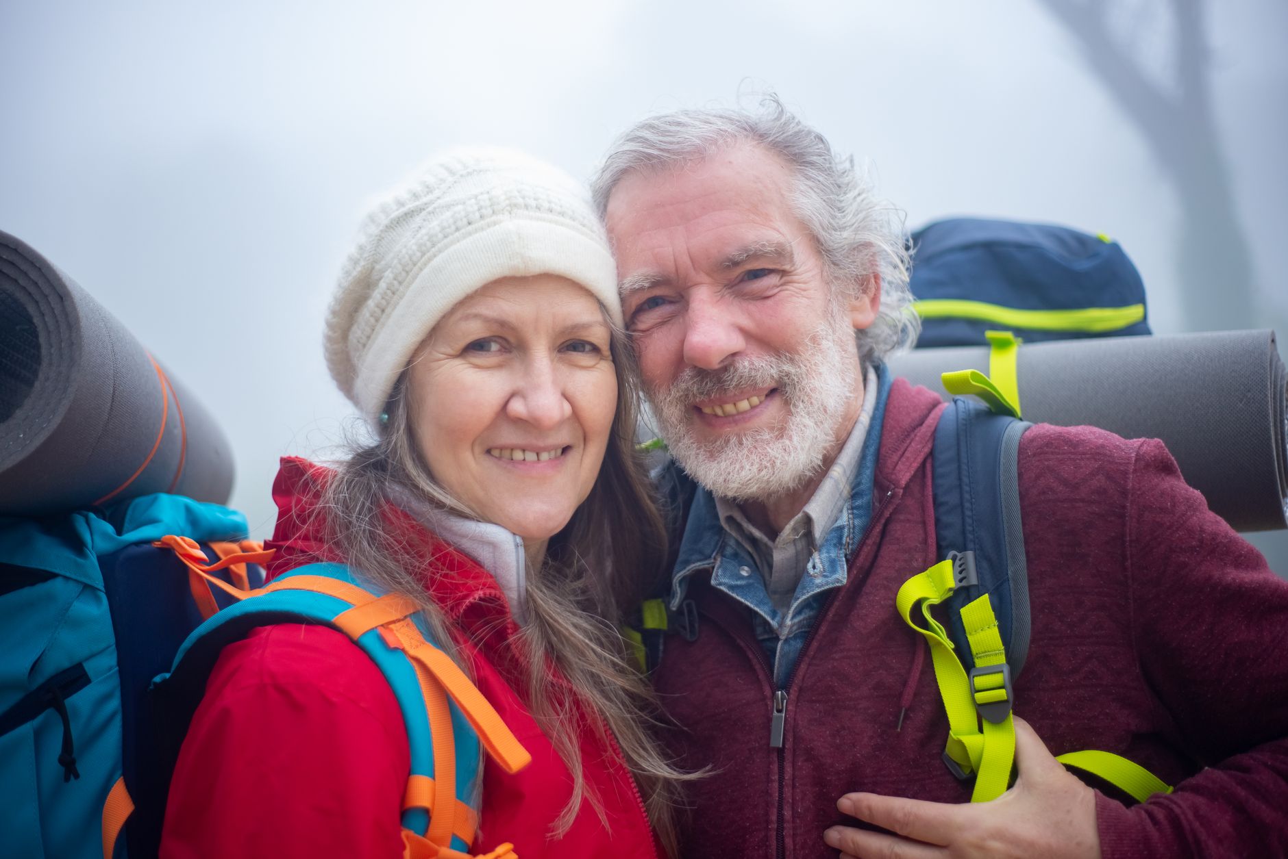 A senior couple hiking outdoors with backpacks on a misty trail — Longevity & Healthspan
