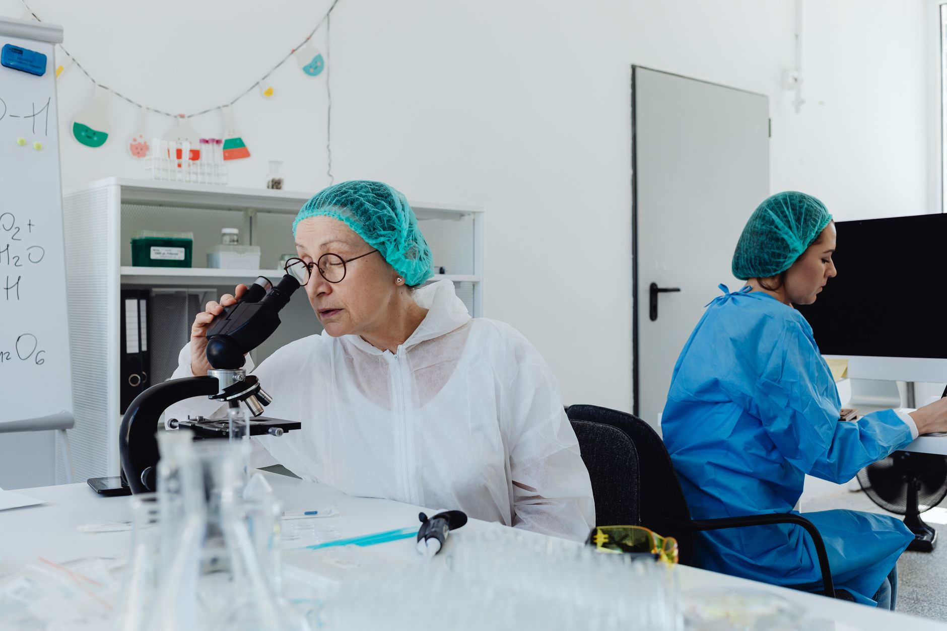 Scientists in coveralls and hair nets conducting research with microscopes and computers in a lab — Longevity & Healthspan