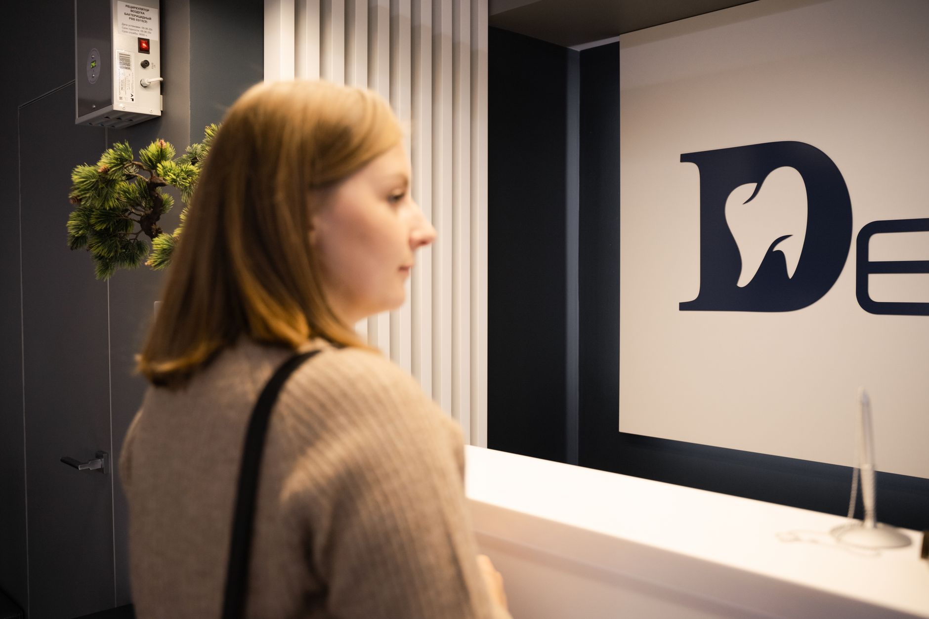 Young woman stands at a dental office reception, side view, casual attire — Healthcare Infrastructure