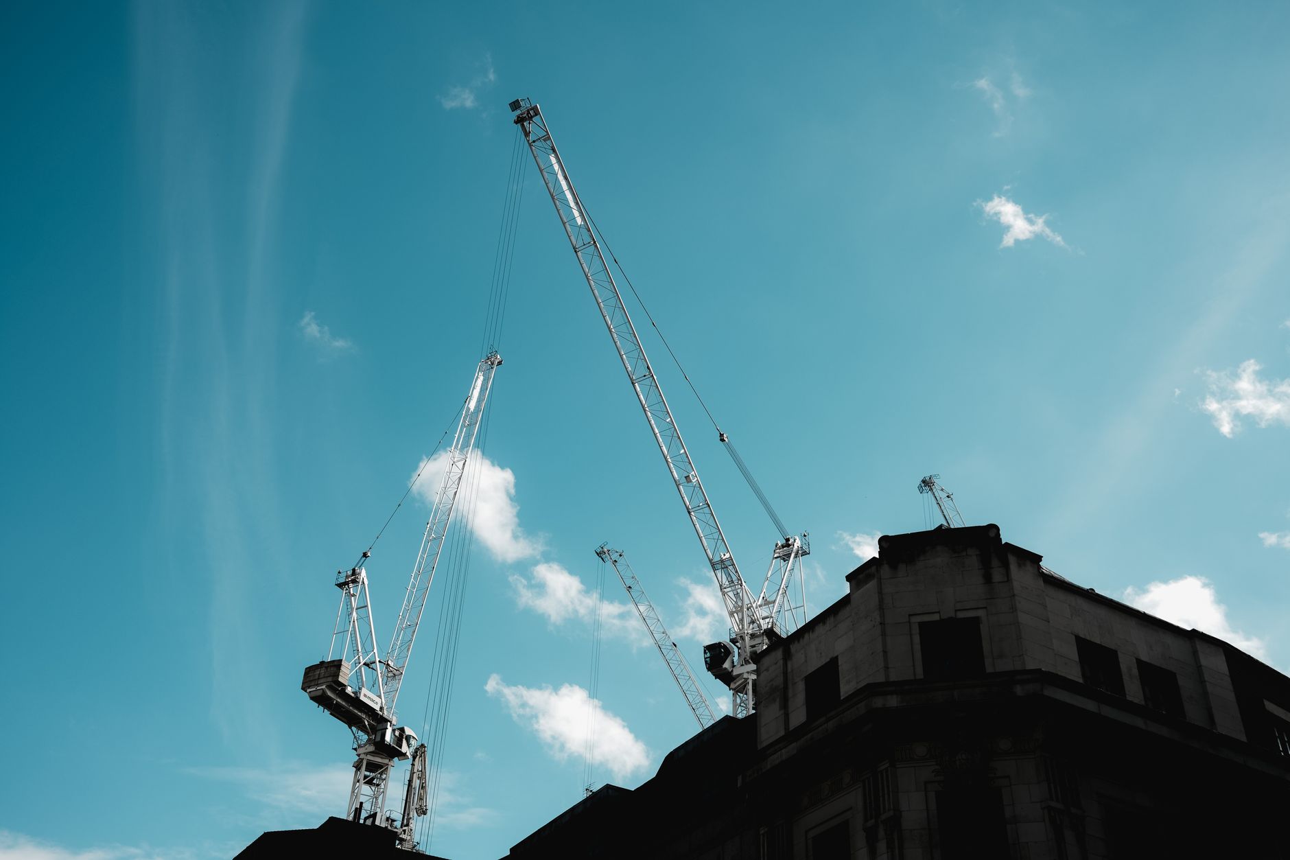 Silhouetted construction cranes extend into a clear blue sky — Healthcare Infrastructure