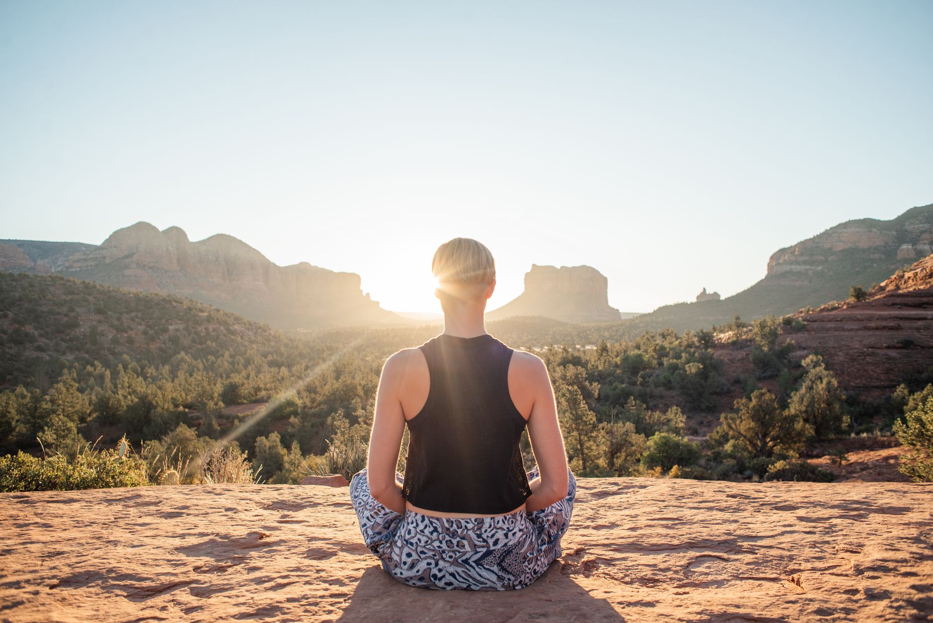 A woman meditating cross-legged on a sunlit clifftop at sunrise — Longevity Tourism & Wellness