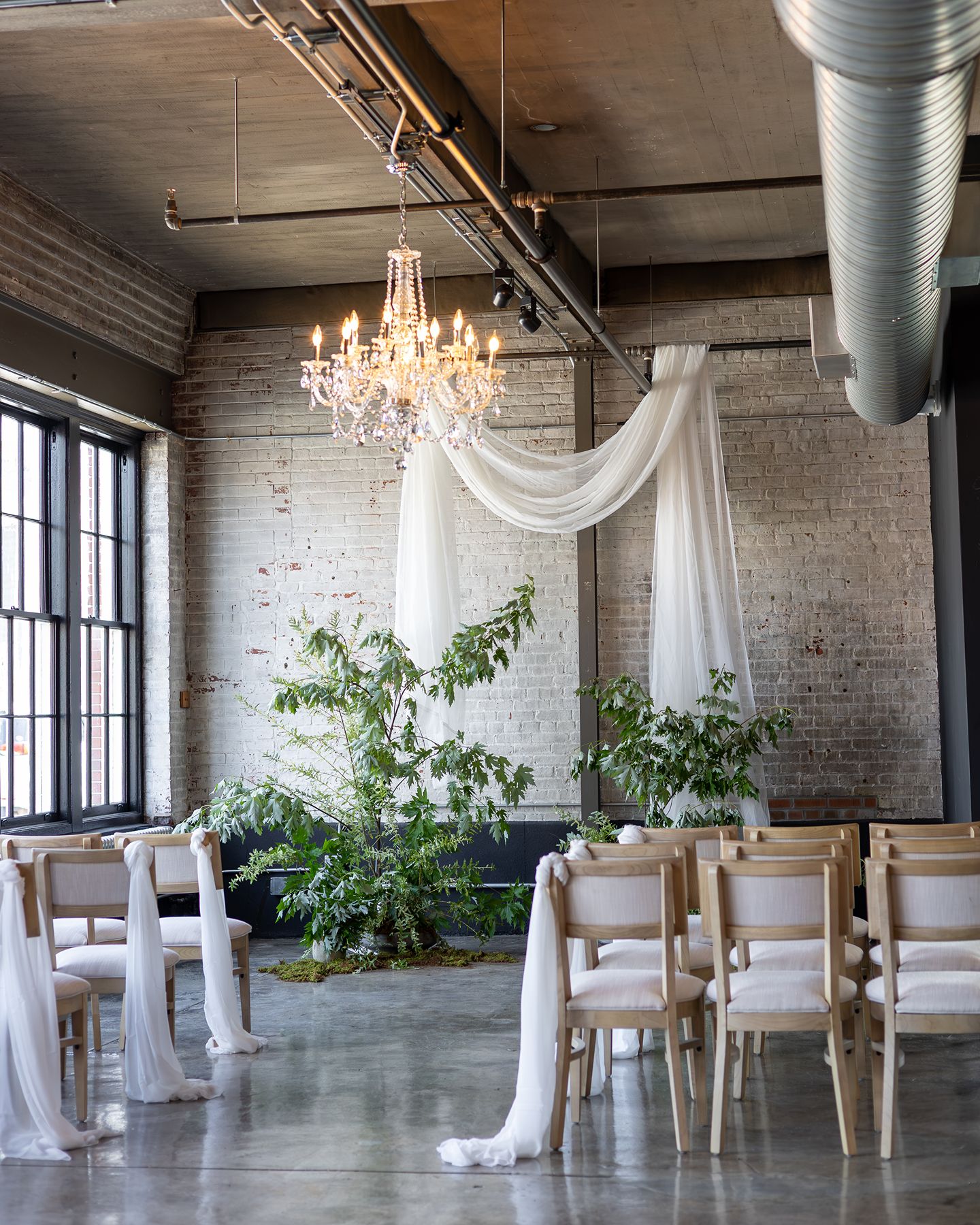 Minimalist wedding ceremony with flowing drapery and natural greenery inside The Bond's industrial wedding venue in downtown York, Pennsylvania.