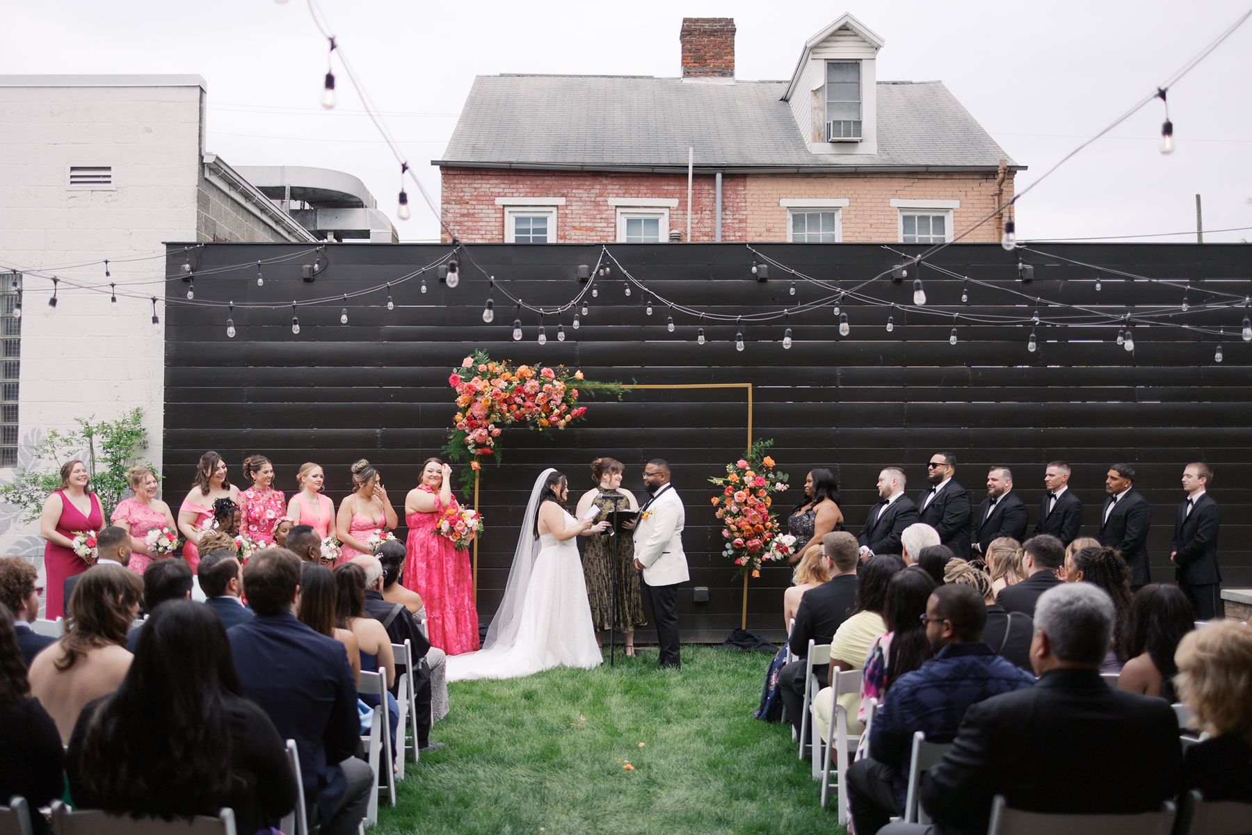 Outdoor wedding ceremony in The Bond's private garden featuring a modern black backdrop, colorful floral arch, and string lights in downtown York, PA.