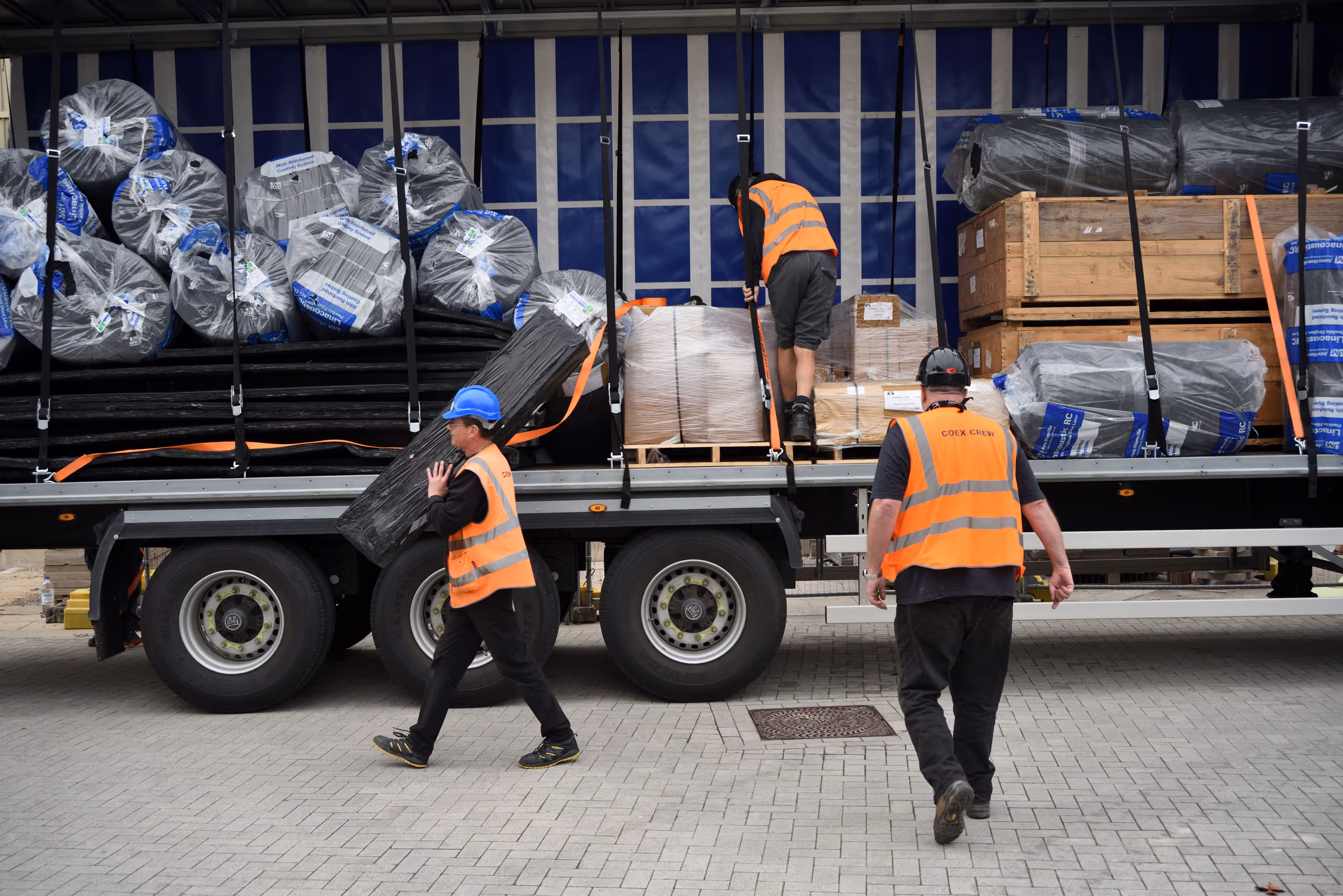 Workers in orange hi-vis vests unloading construction materials from delivery truck