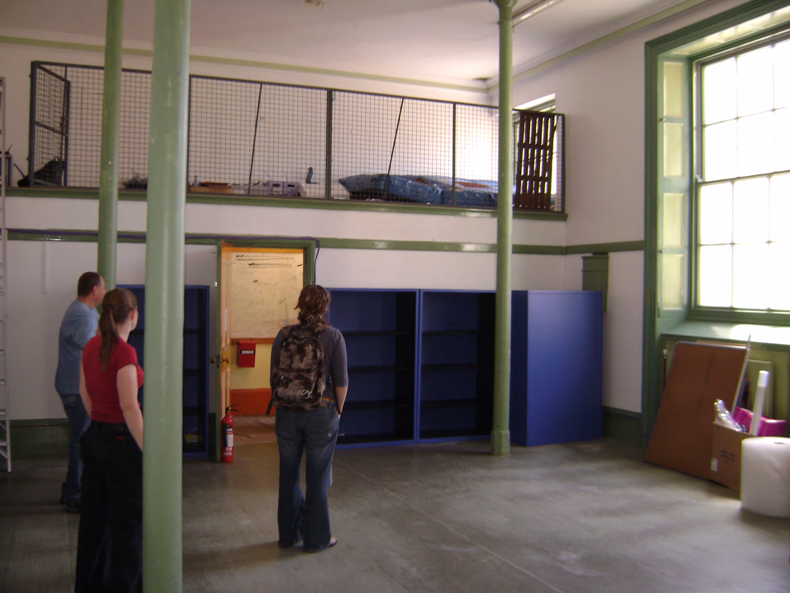 Multi-level interior space with green columns, mezzanine level, and people observing renovation work