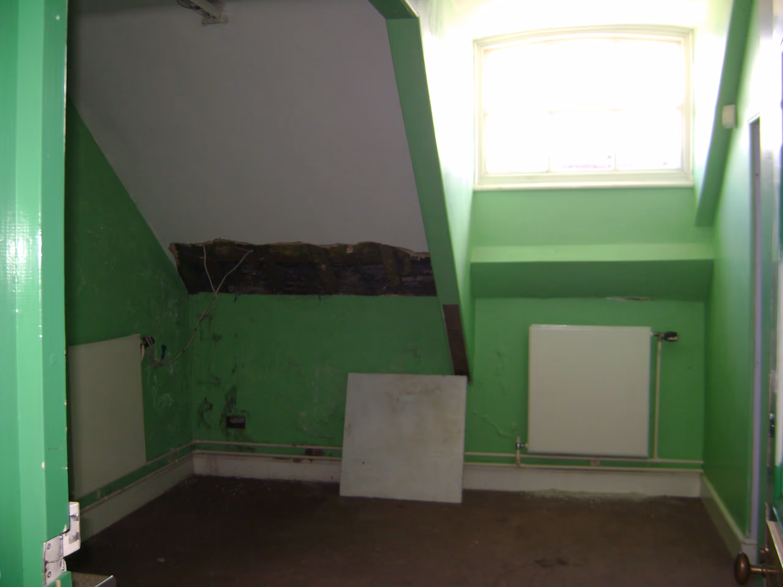 Green-painted interior room under renovation showing damaged ceiling and exposed structural elements