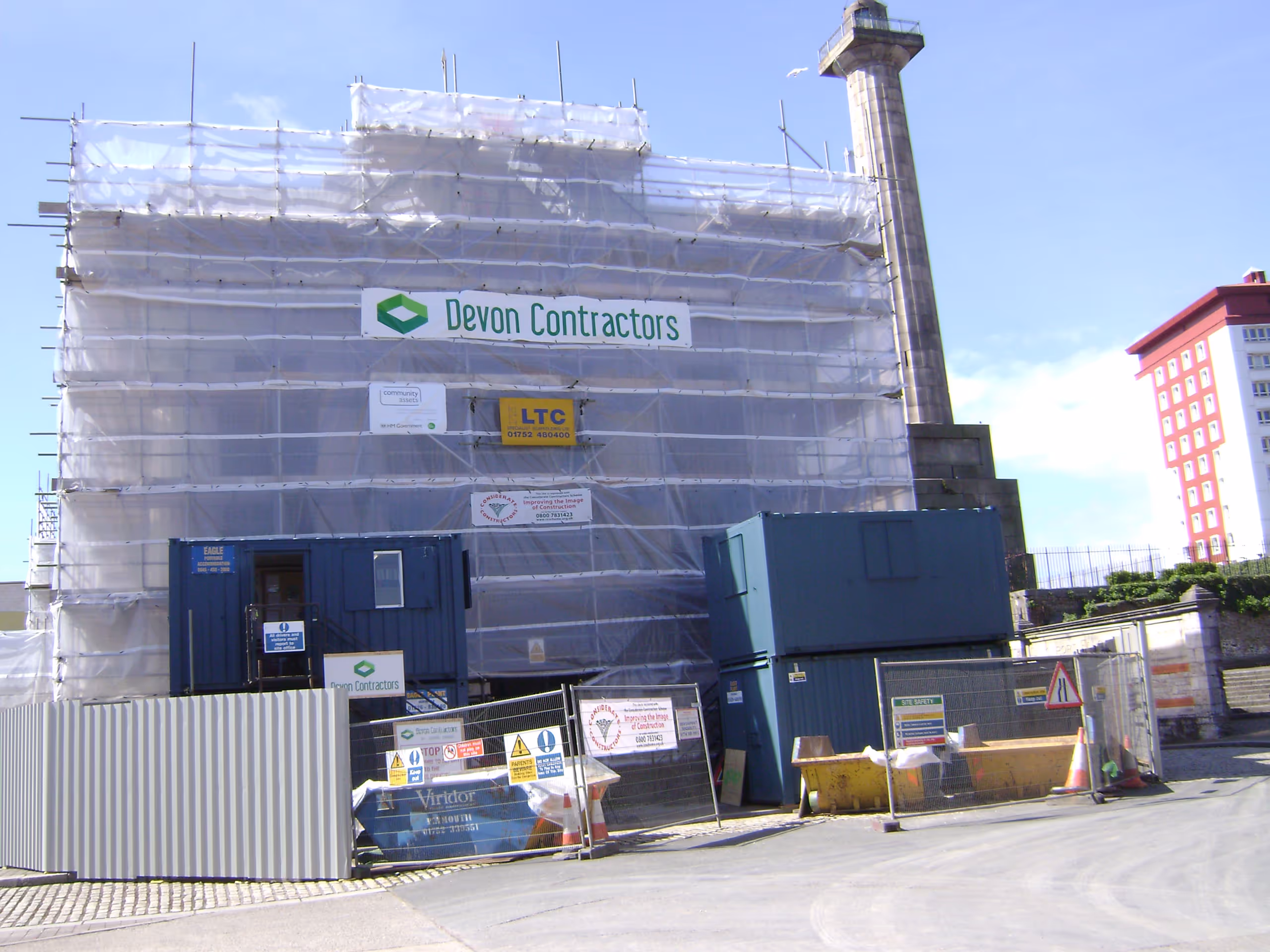 uilding exterior covered in scaffolding and protective sheeting with "Devon Contractors" signage visible