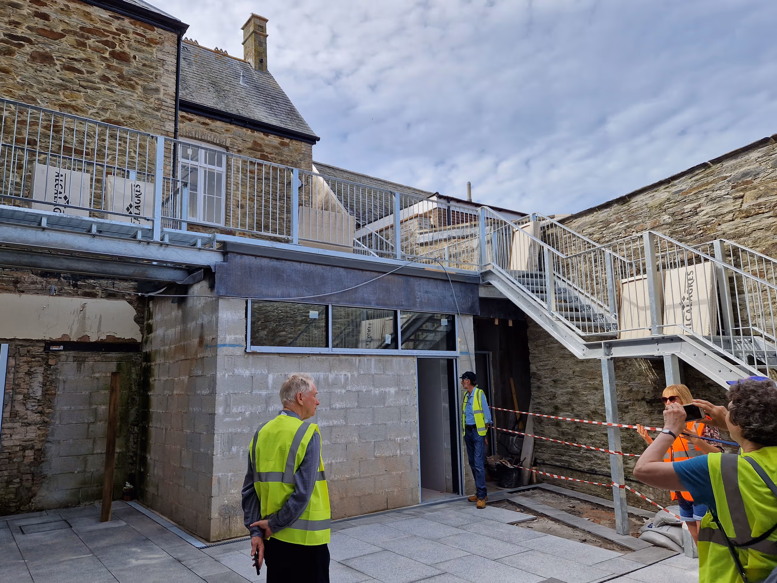 Exterior view of historic stone building with new metal stairs and balcony addition during renovation