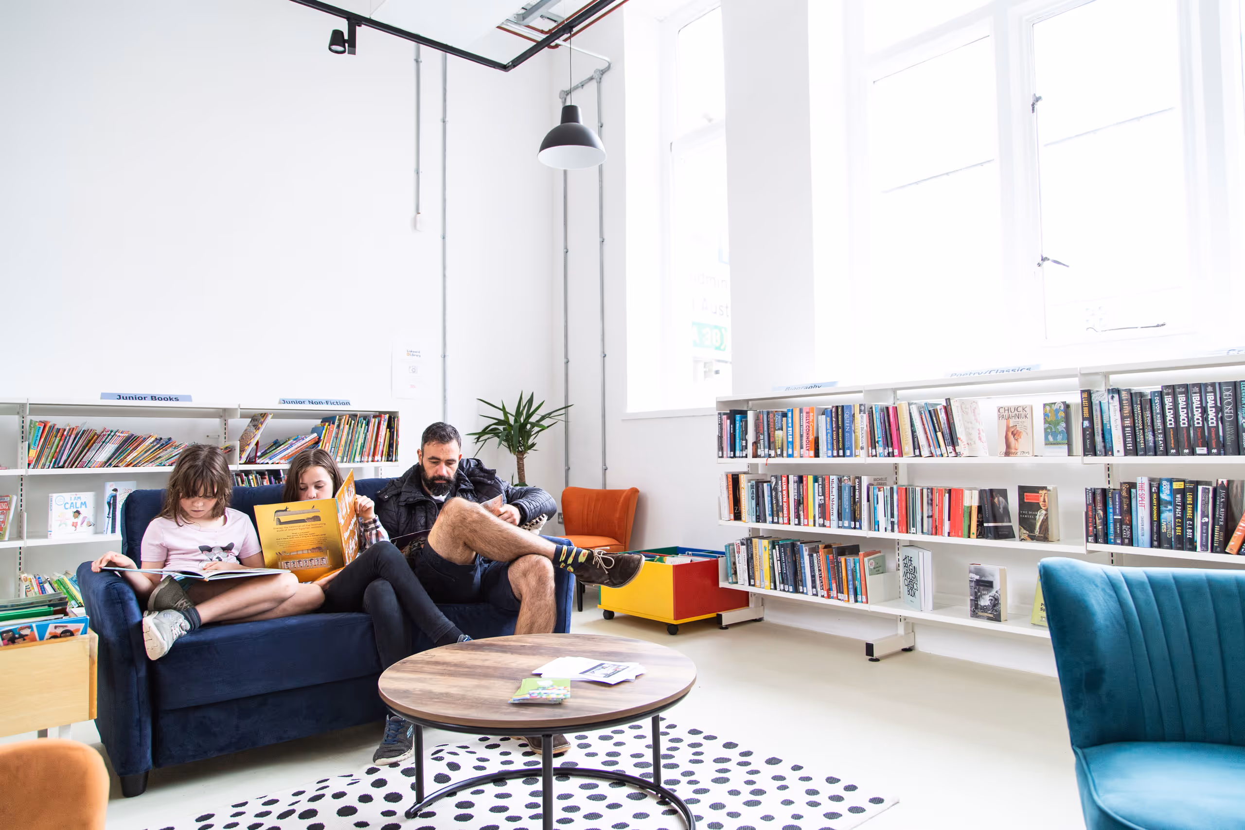 Family reading time with father and two children on navy sofa surrounded by organised book collections