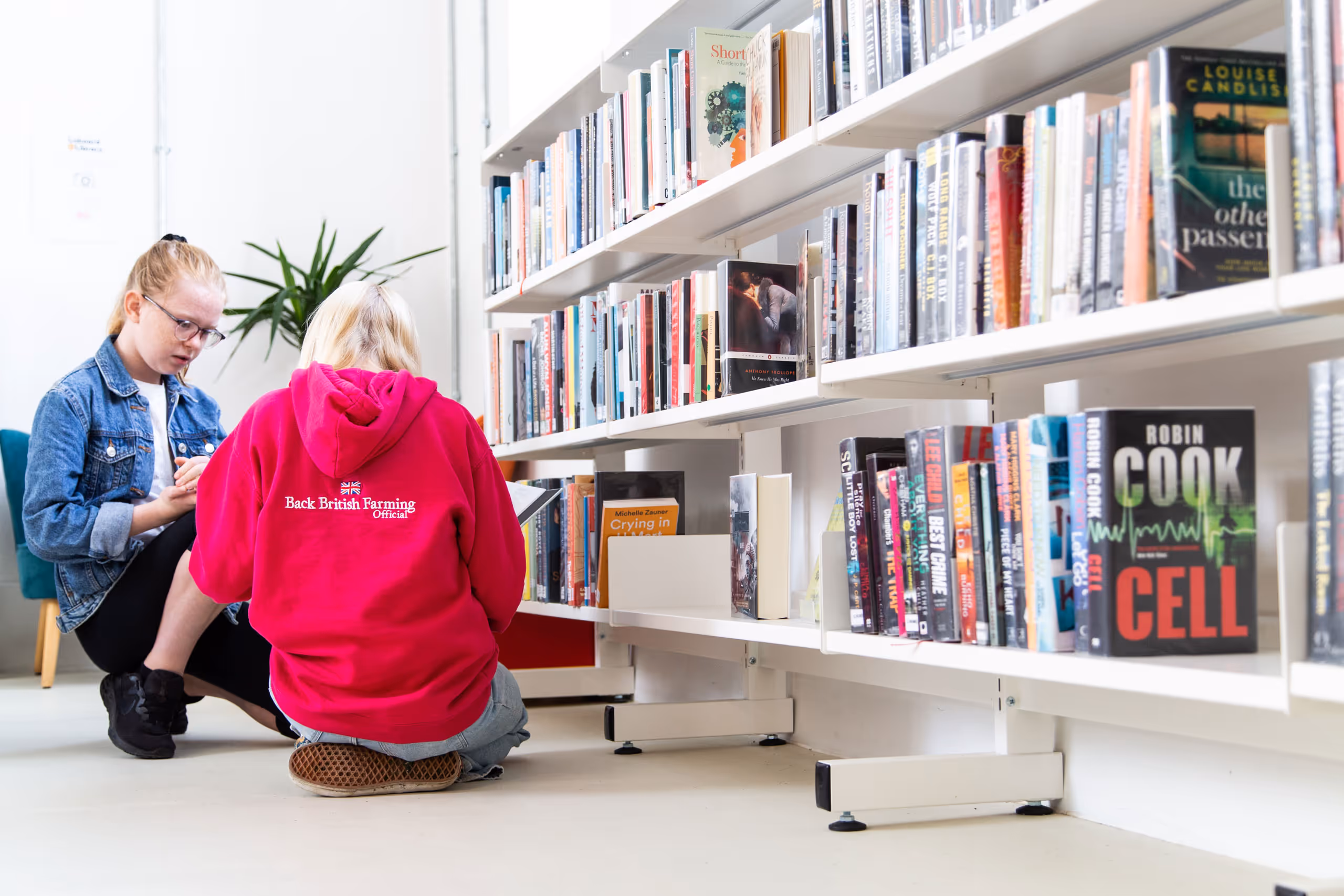 Two young people browsing lower book shelves in bright modern library space