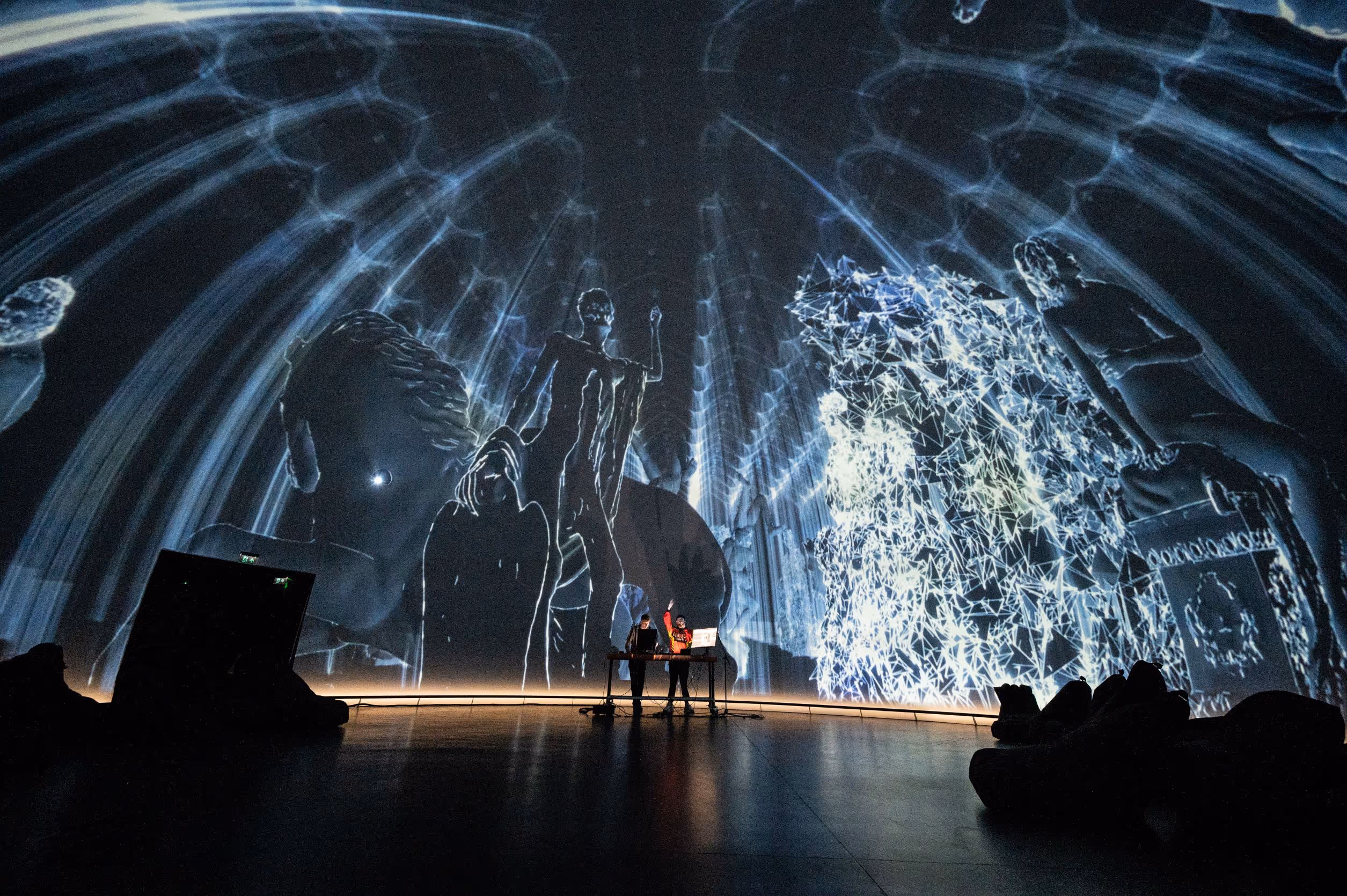Spectacular 360-degree projection dome displaying blue abstract digital art with silhouetted figures presenting to seated audience