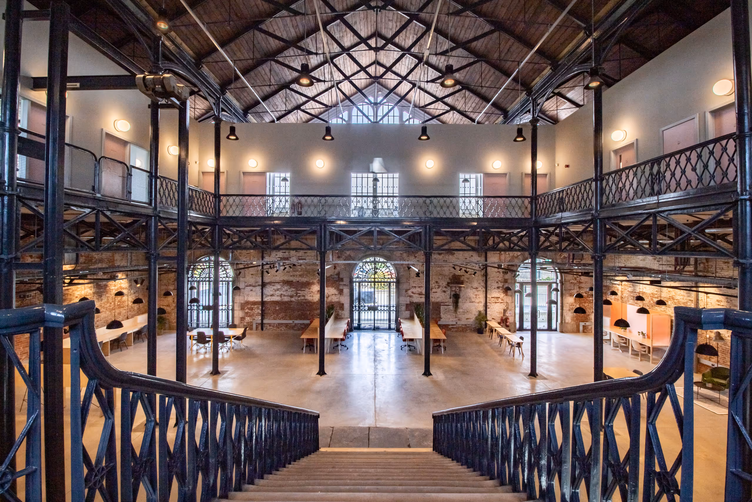 Dramatic two-story workspace viewed from ornate Victorian iron staircase, showing open floor plan with workstations and arched windows