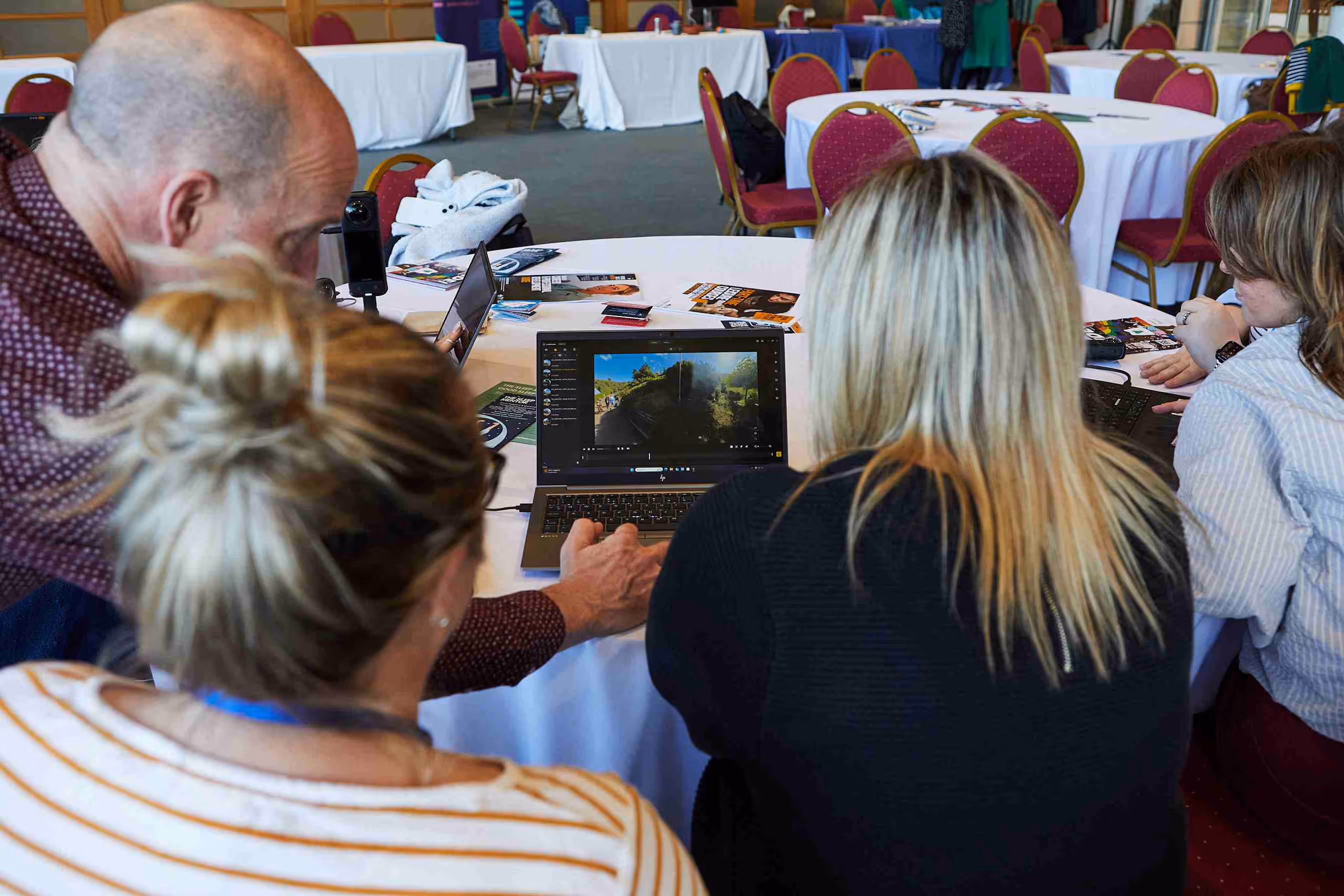 Small group examining laptop screen showing landscape imagery in conference room setting