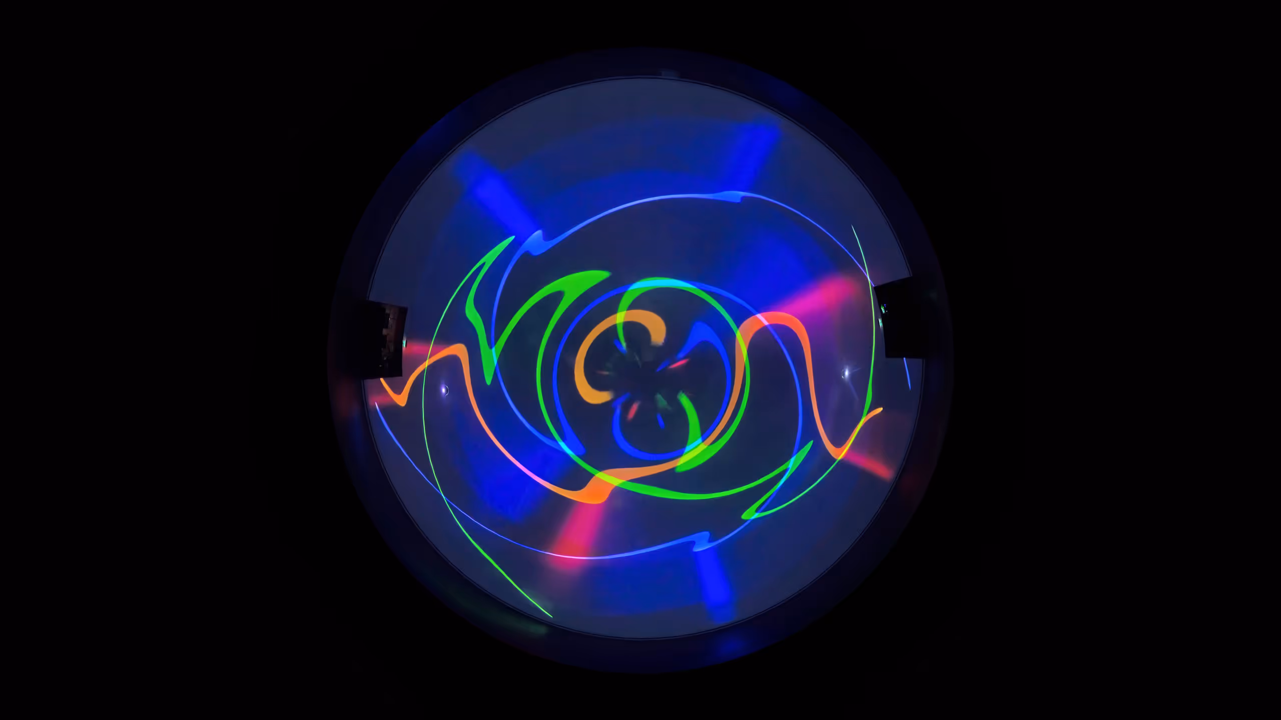 Circular projection showing swirling multicolored light patterns in dark immersive space