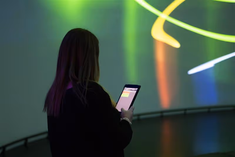 Person using tablet device in darkened room with colorful projected light trails