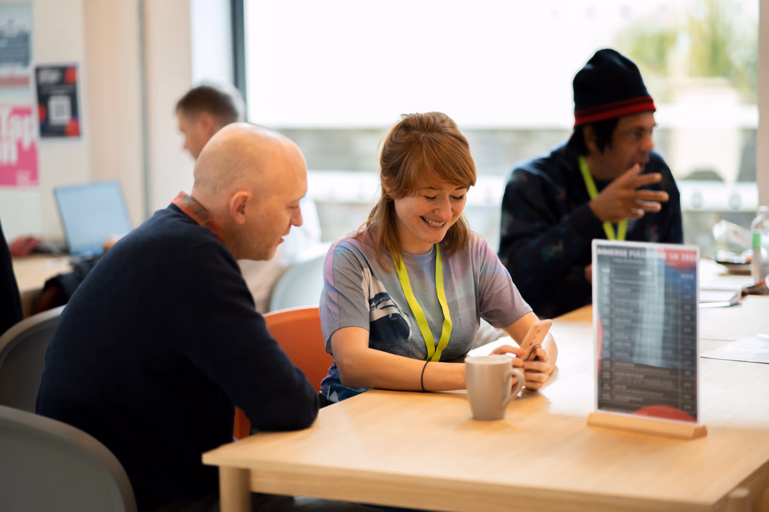 Two people having informal conversation at cafe table, one wearing conference lanyard