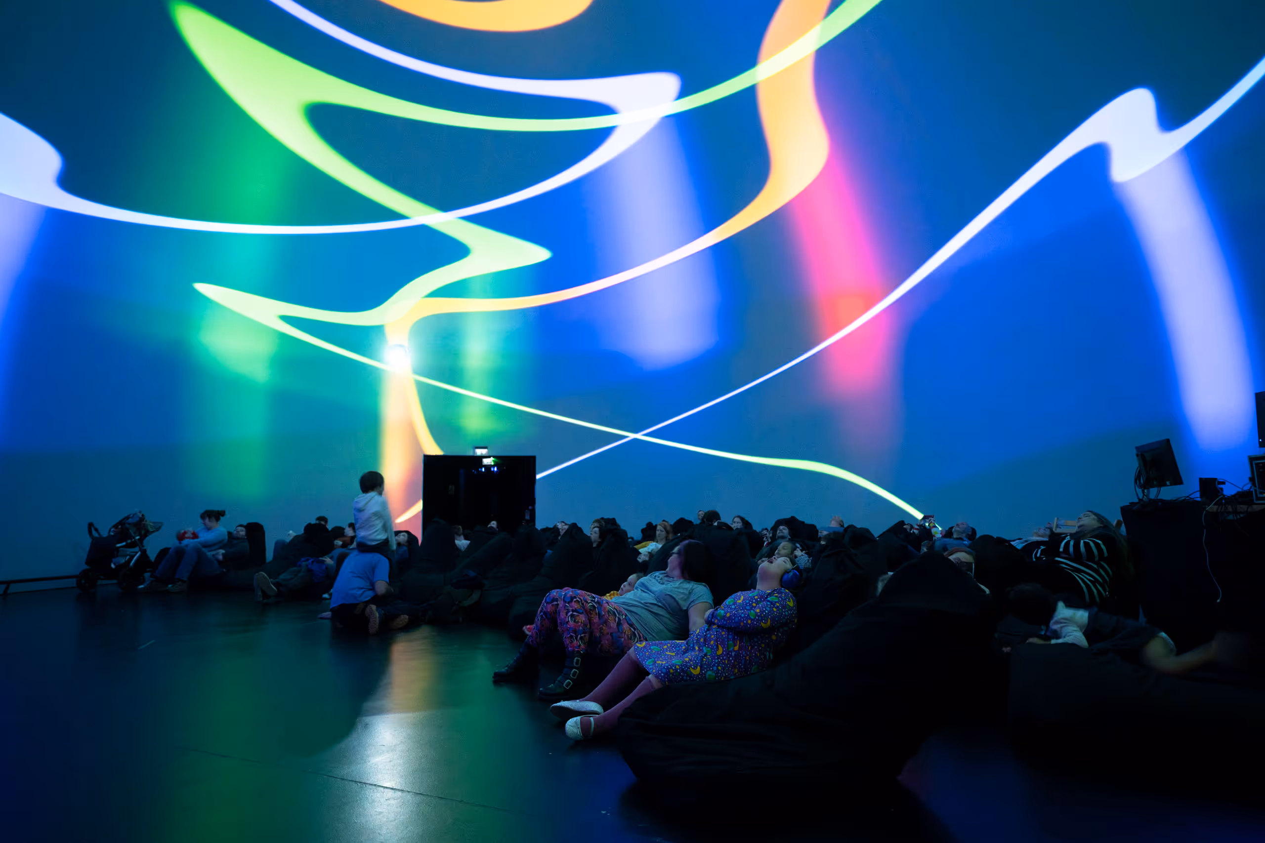 People lying on floor experiencing immersive light installation with flowing multicolored patterns