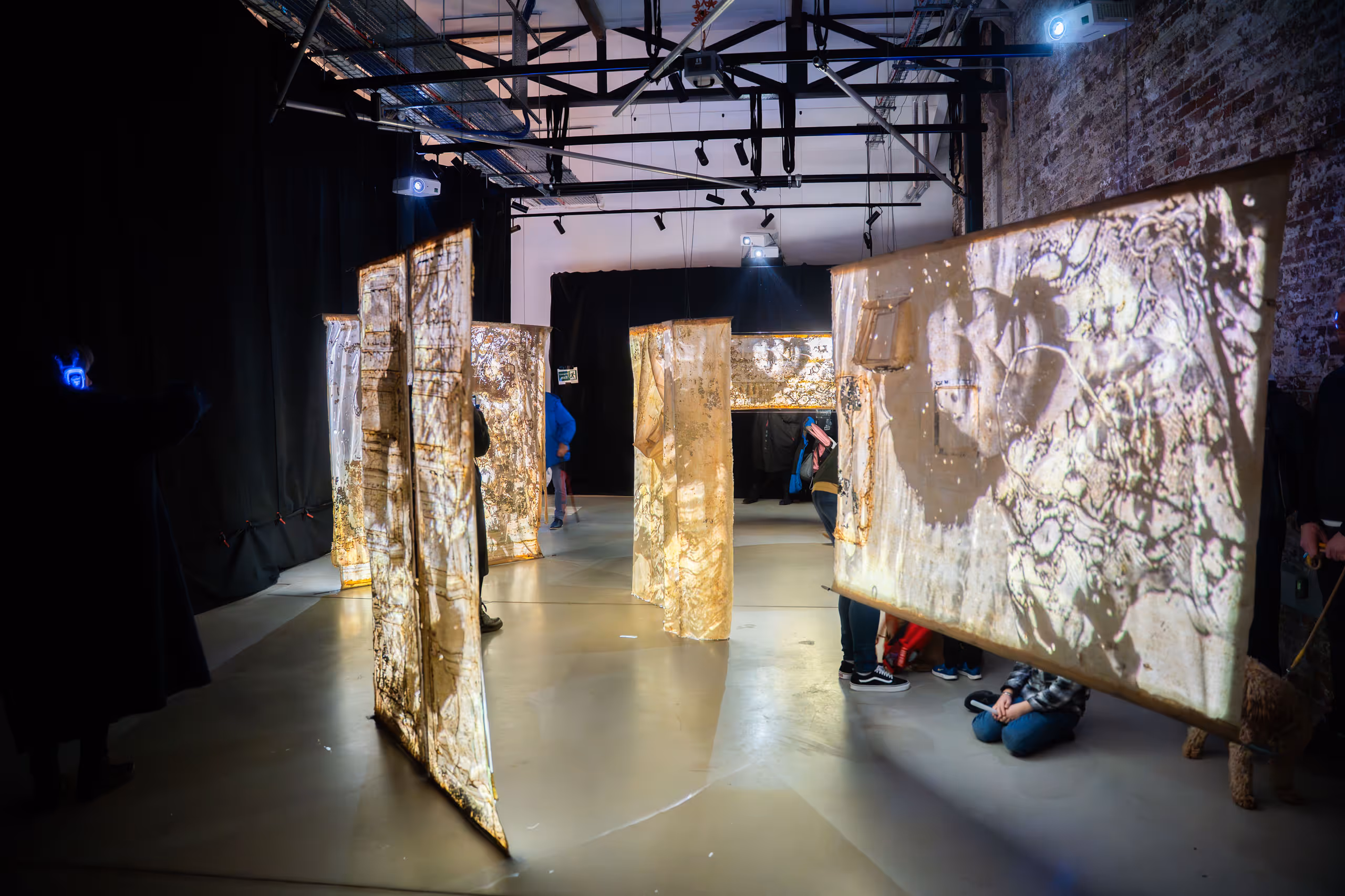 Large-scale digital art installation with projected imagery on suspended panels in dark warehouse space