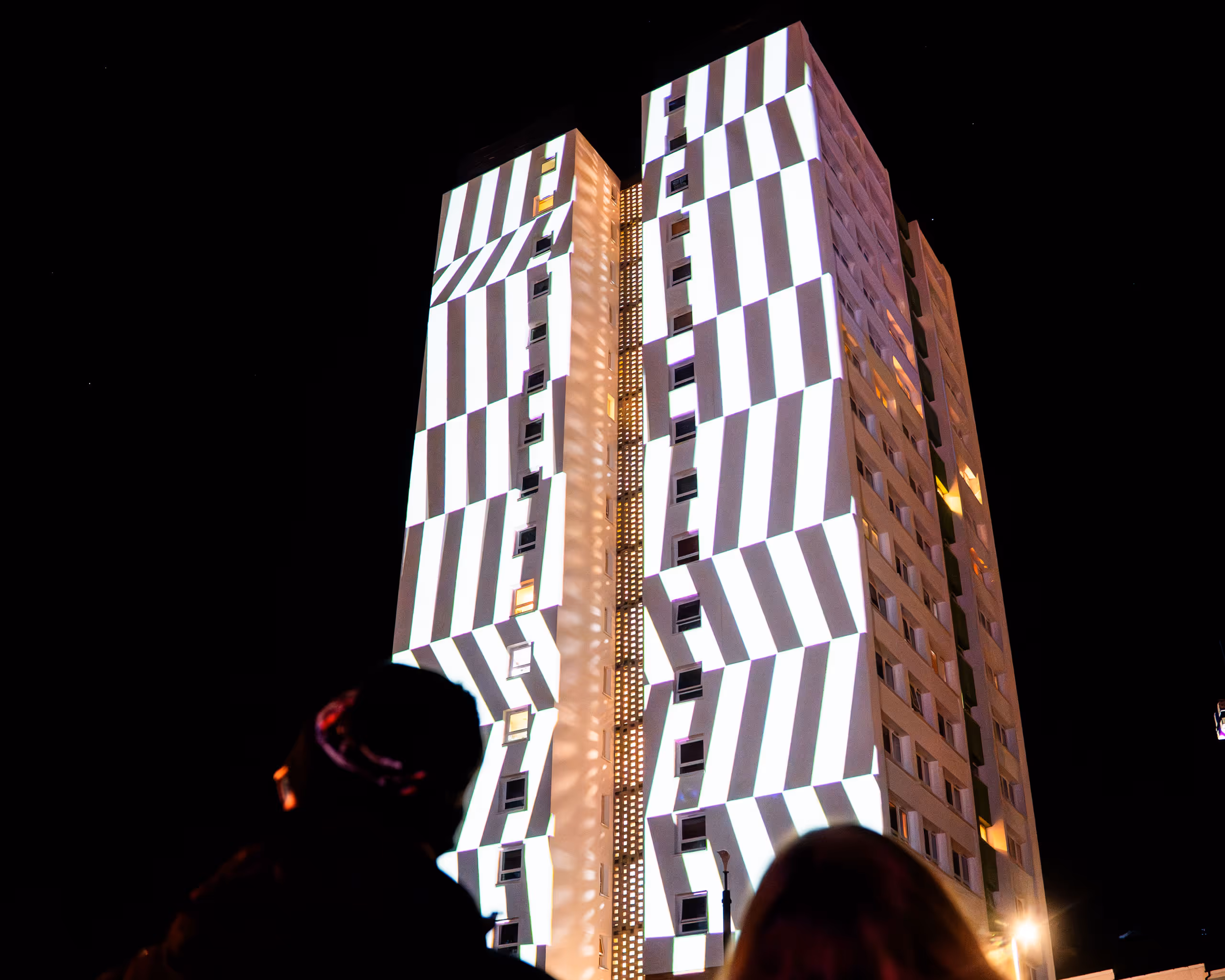 Tall building illuminated with dramatic striped light projection at nighttime festival event