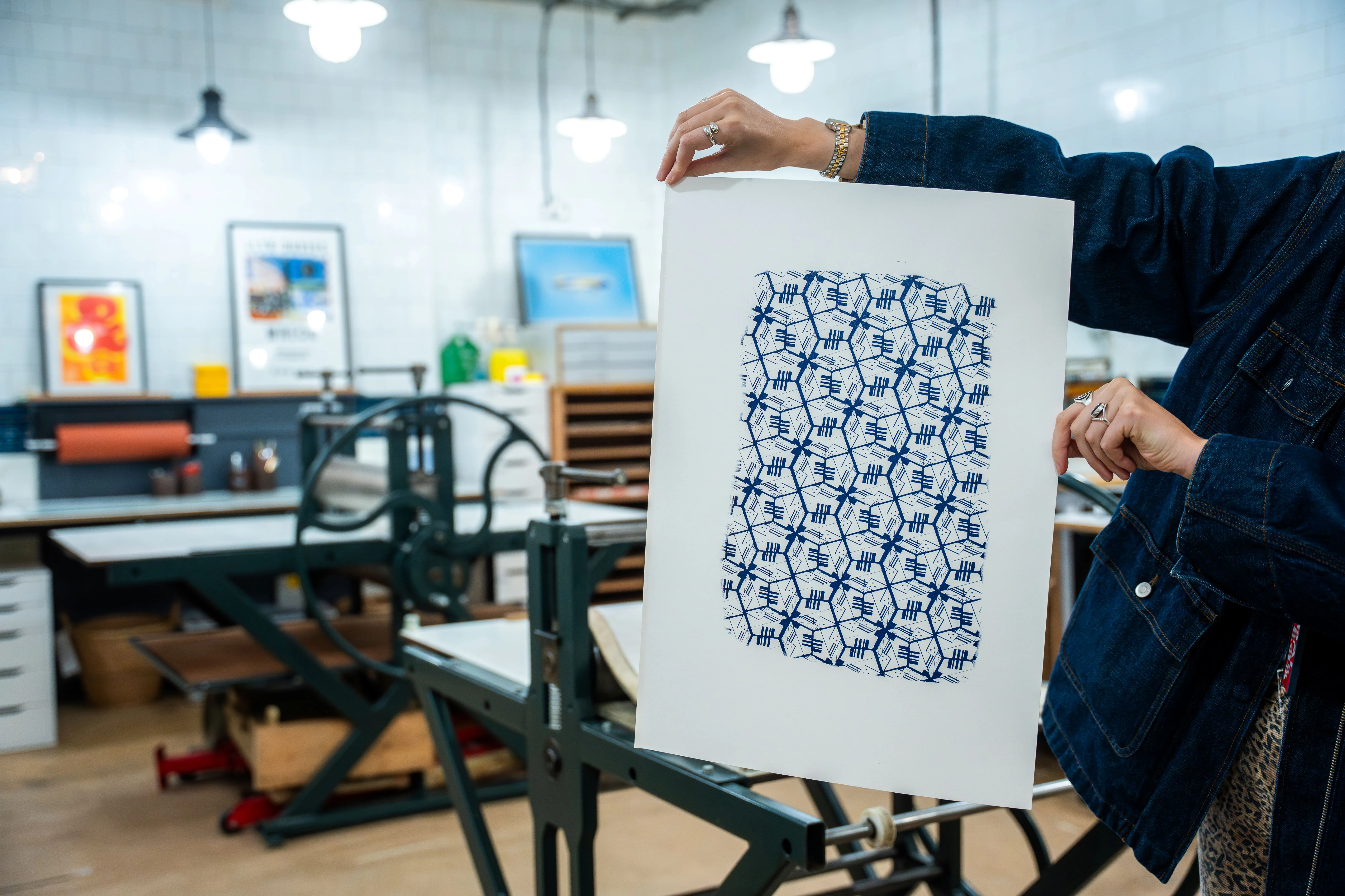 Person holding a white sheet with a blue geometric block print pattern in a printmaking studio.
