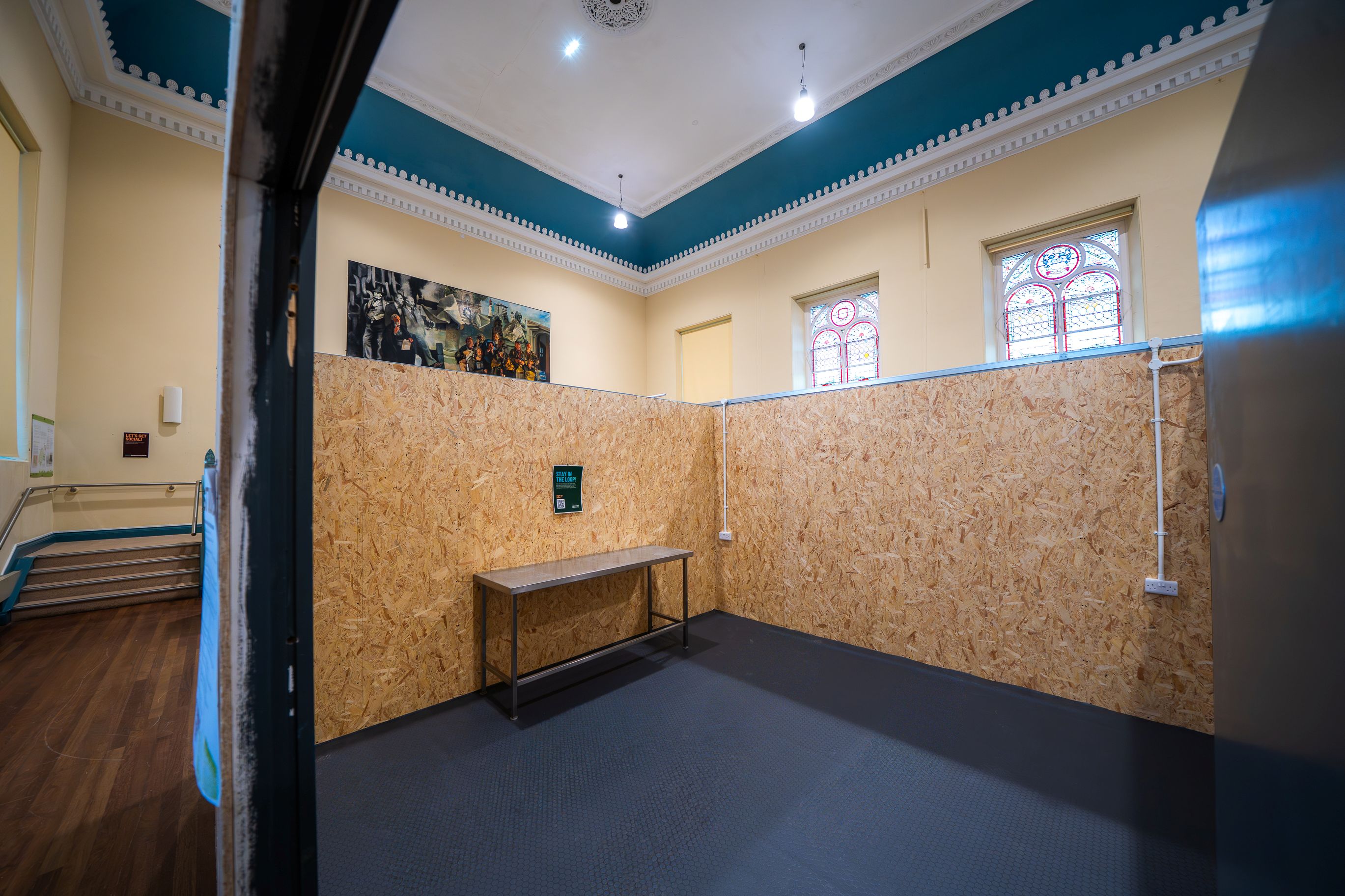 Empty room with wood-patterned paneled walls, a metal table, and stained glass windows near the ceiling.