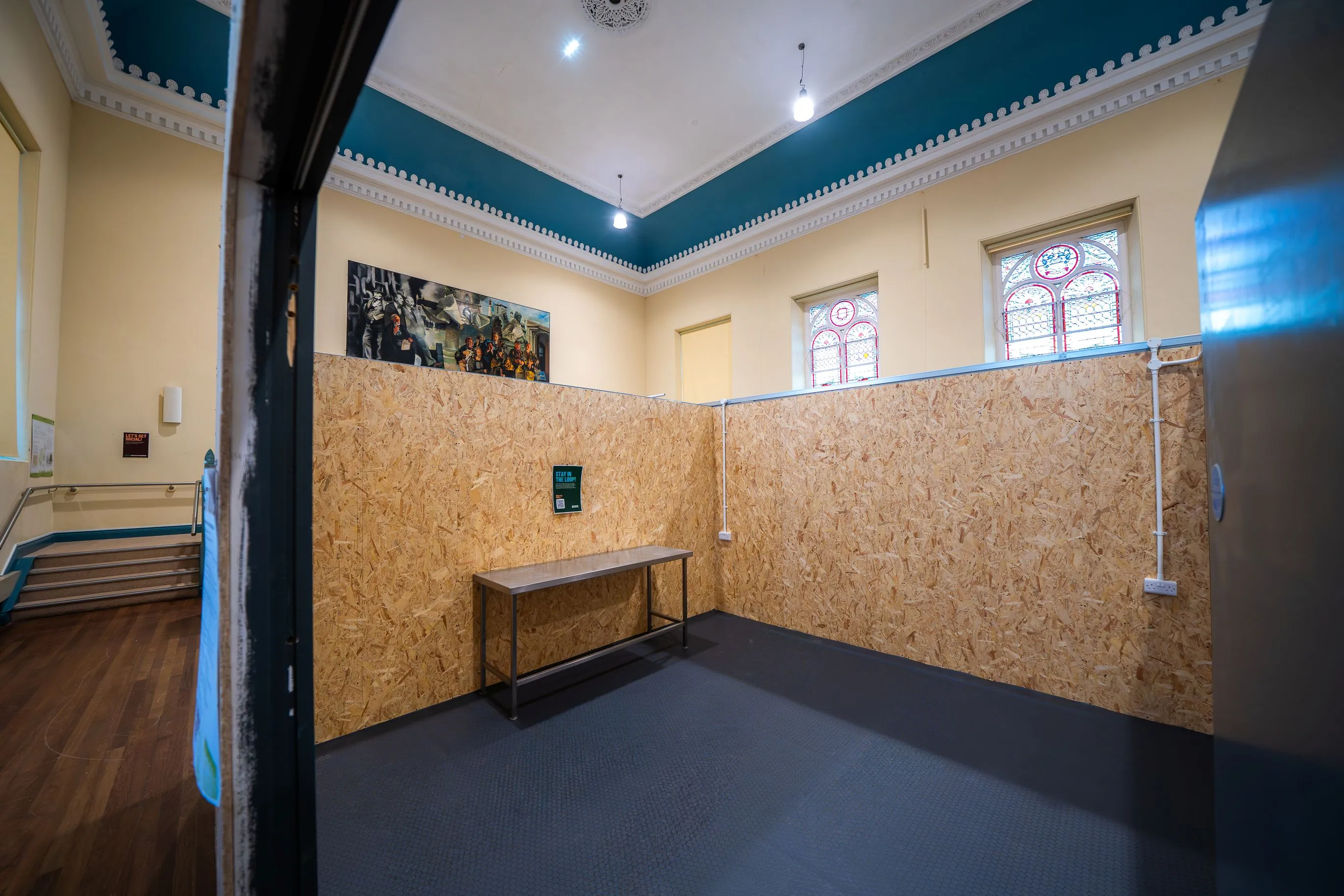 Empty room with wood-patterned paneled walls, a metal table, and stained glass windows near the ceiling.