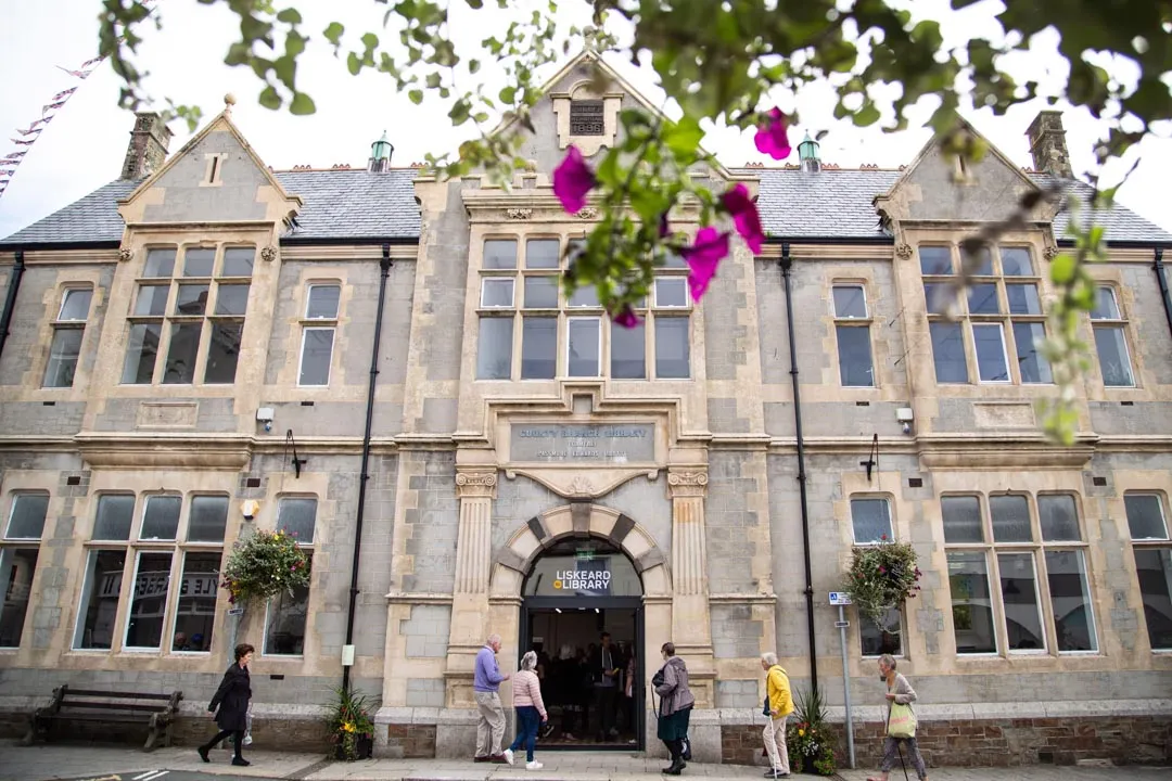 Liskeard Library, a historic Victorian stone library building with ornate entrance archway and people walking outside