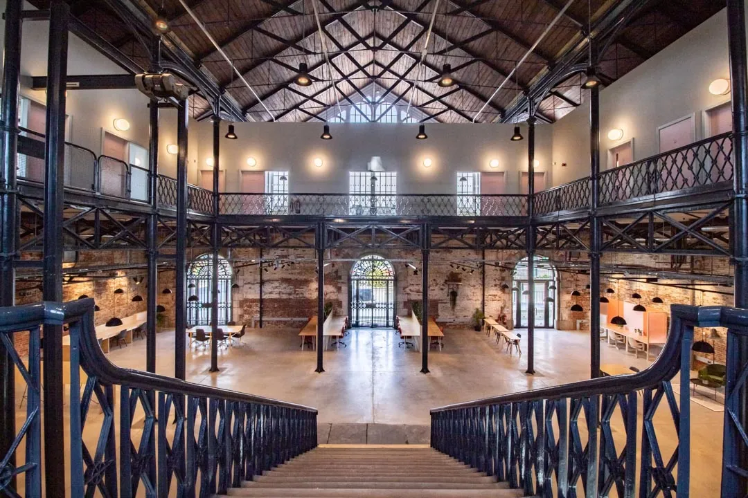 Dramatic two-story workspace viewed from ornate Victorian iron staircase, showing open floor plan with workstations and arched windows