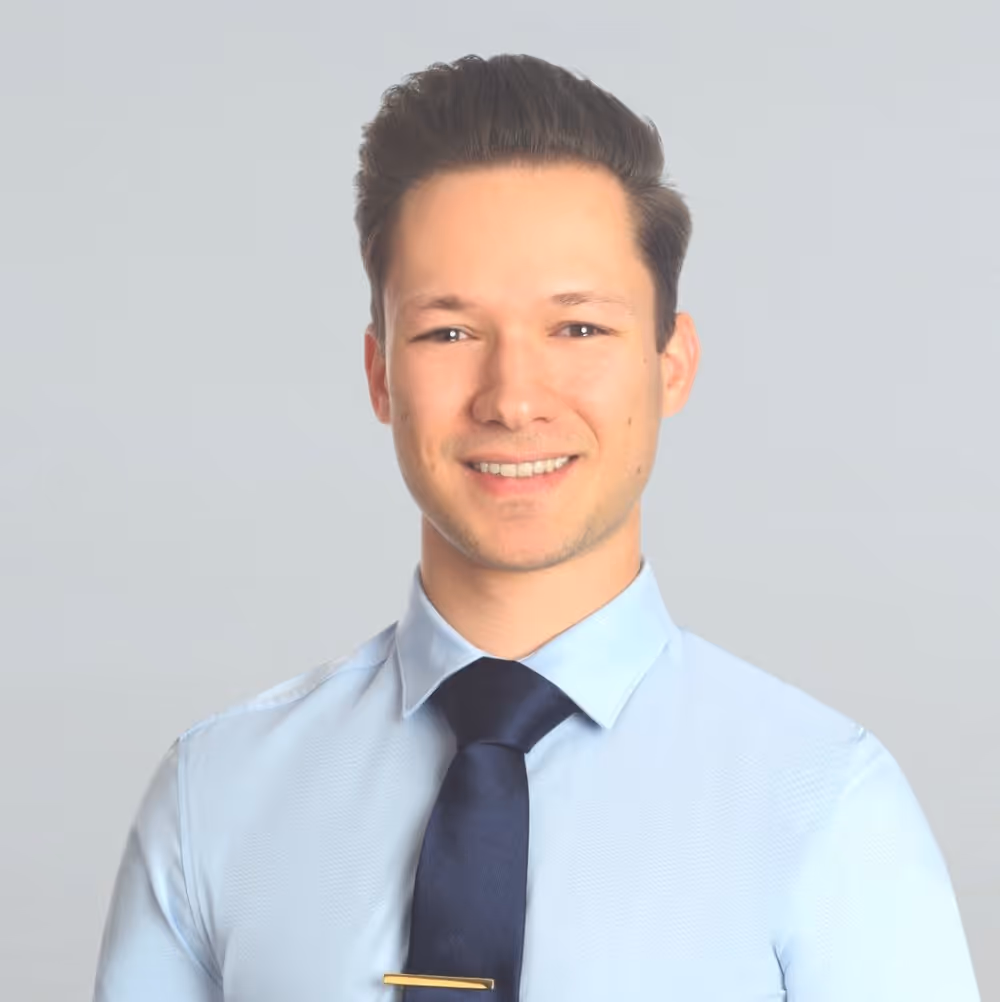 Portrait of a smiling man with dark brown hair wearing a light blue shirt and a dark blue tie.